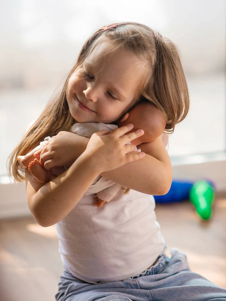 A little girl holds a reborn baby doll warmly in her arms