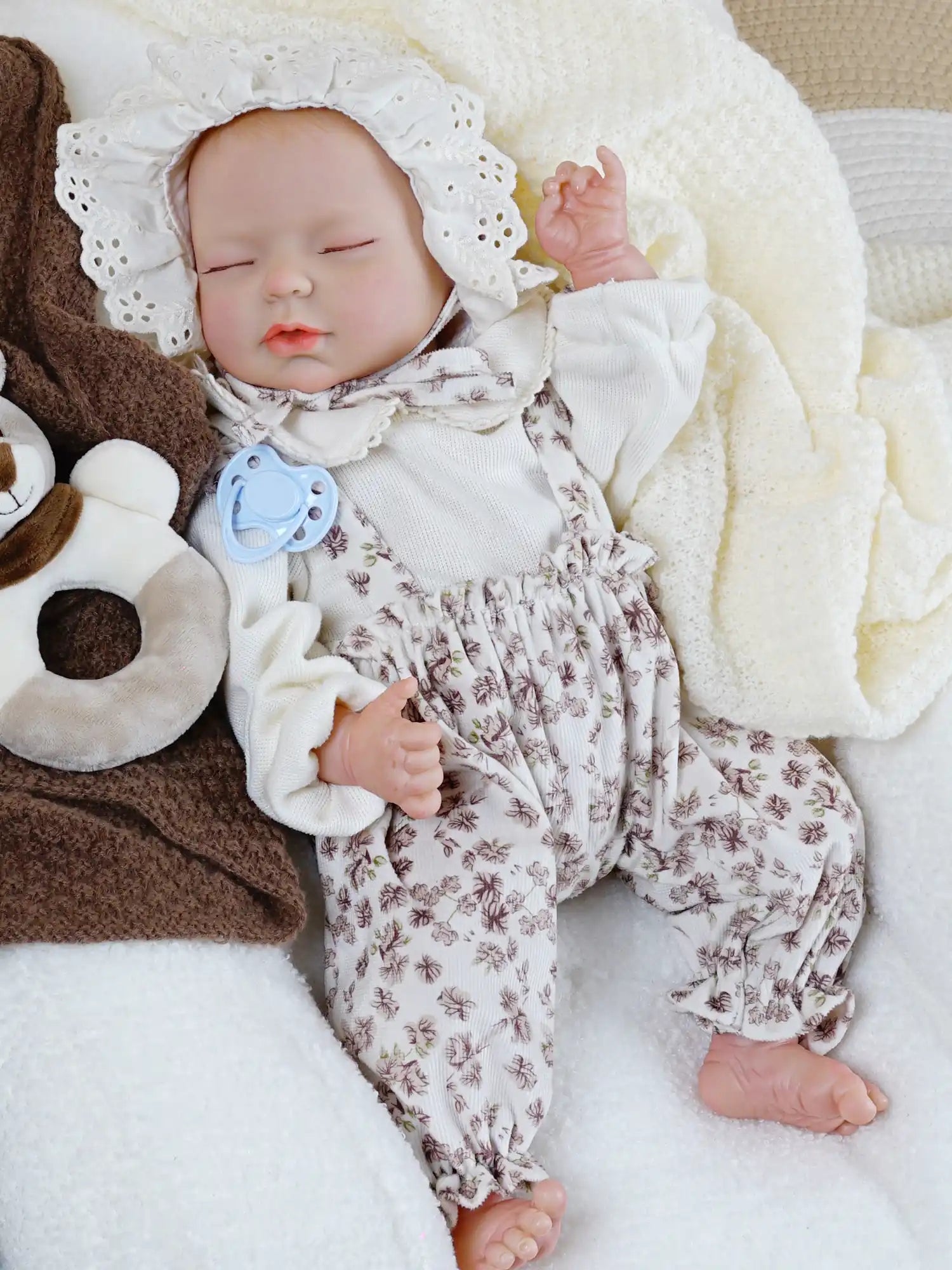 Sleeping reborn baby doll with floral jumpsuit and lace bonnet.