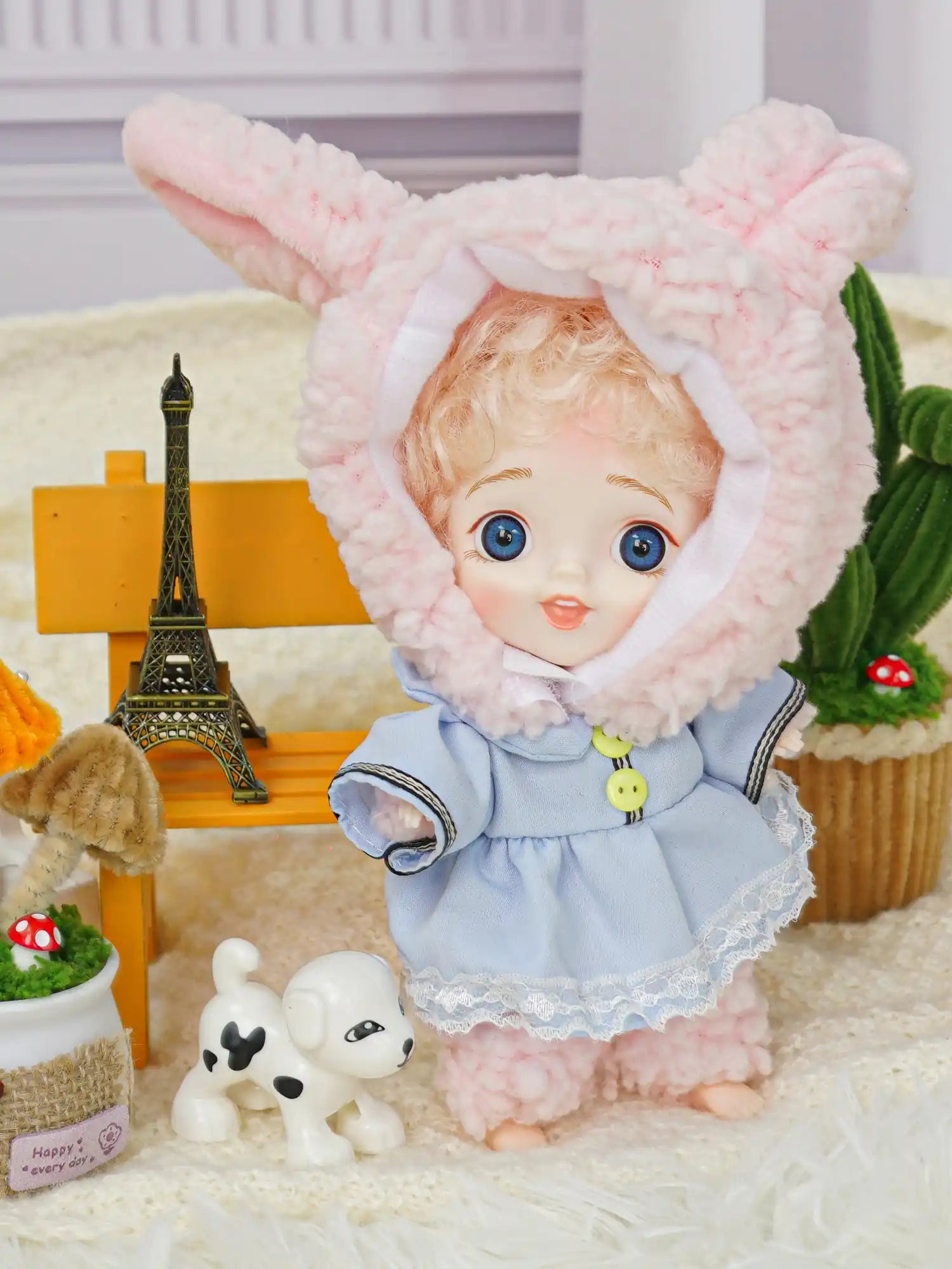BJD with curly hair, blue eyes, bunny ears, and playful companions.