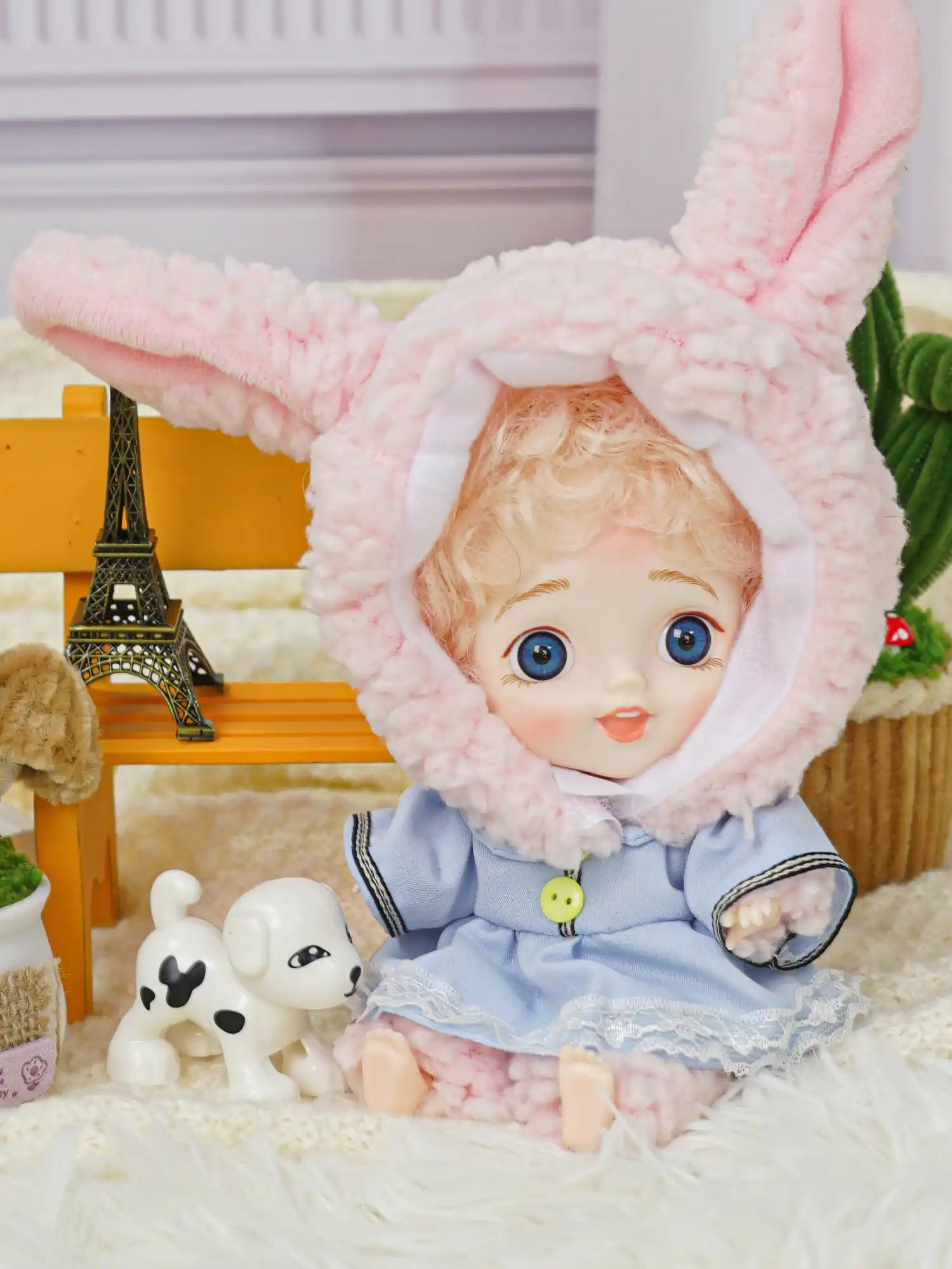 BJD with golden curls in a bunny outfit, next to a miniature Parisian landmark.