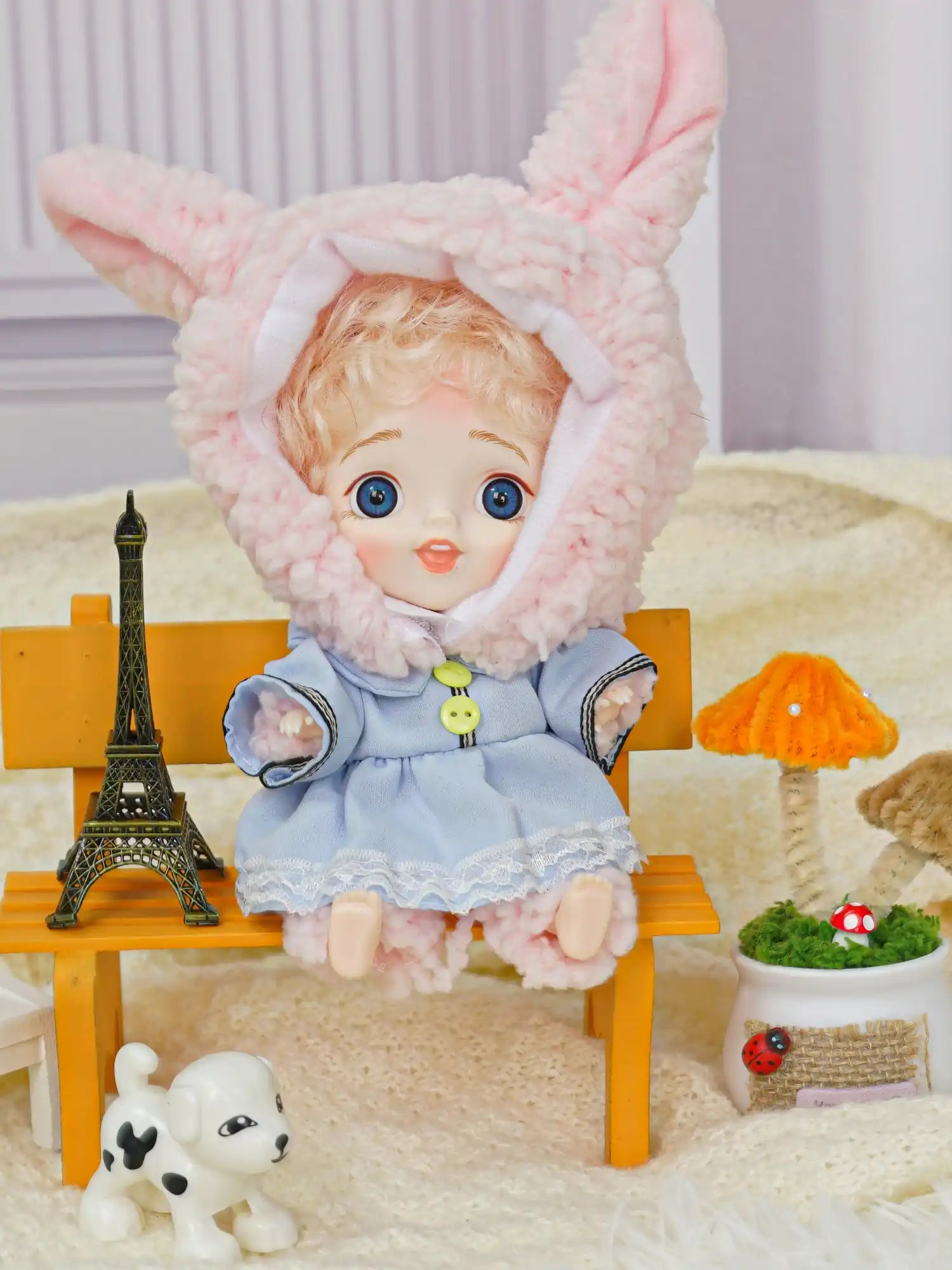 BJD with curly blonde hair in rabbit attire with a toy pup and Eiffel Tower setting.