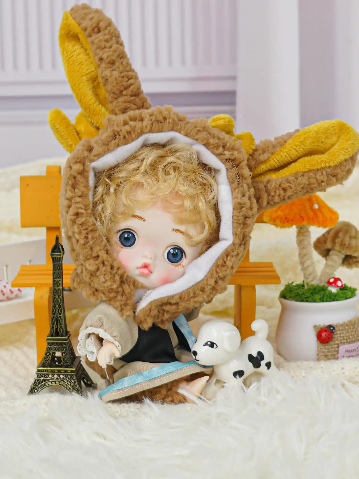 Charming curly-haired doll wearing a bunny costume, seated next to miniature Parisian and animal decorations.