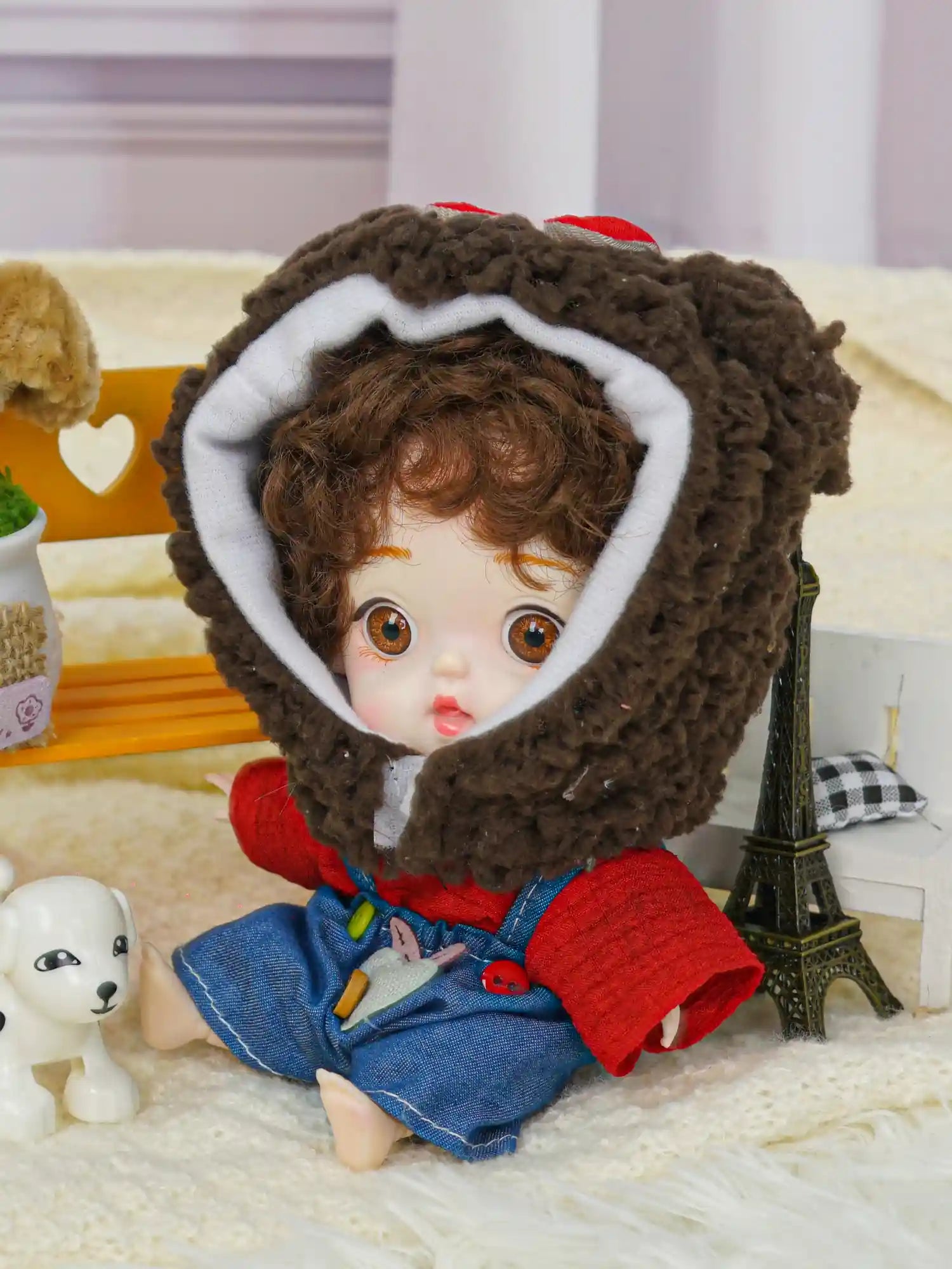 An adorable doll in a bear costume with a whimsical backdrop including a toy Eiffel Tower and playful puppy figure.