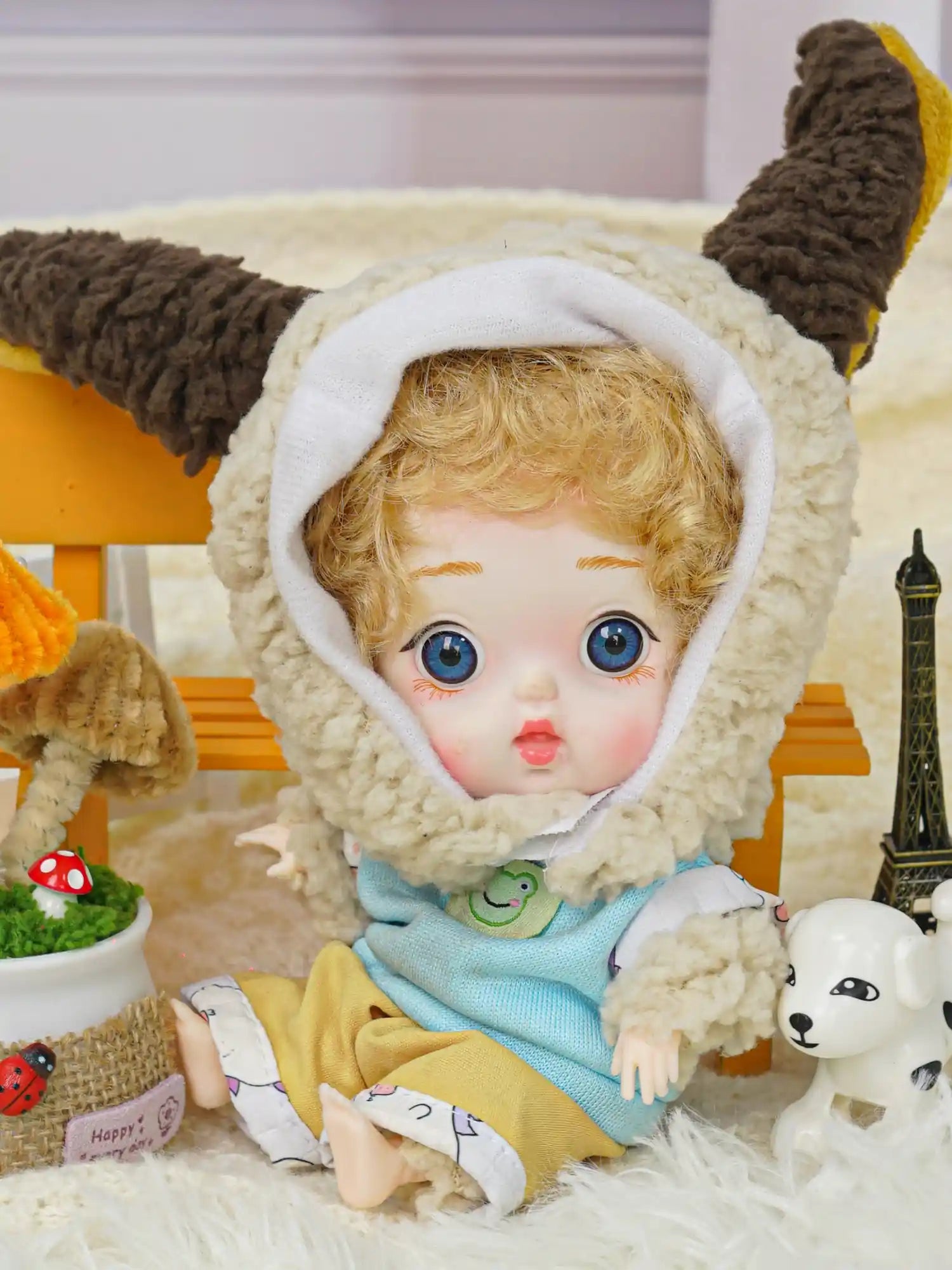 A BJD with bright blue eyes and lamb ears hood stands amidst a scene with a toy dog and a miniature Eiffel Tower.