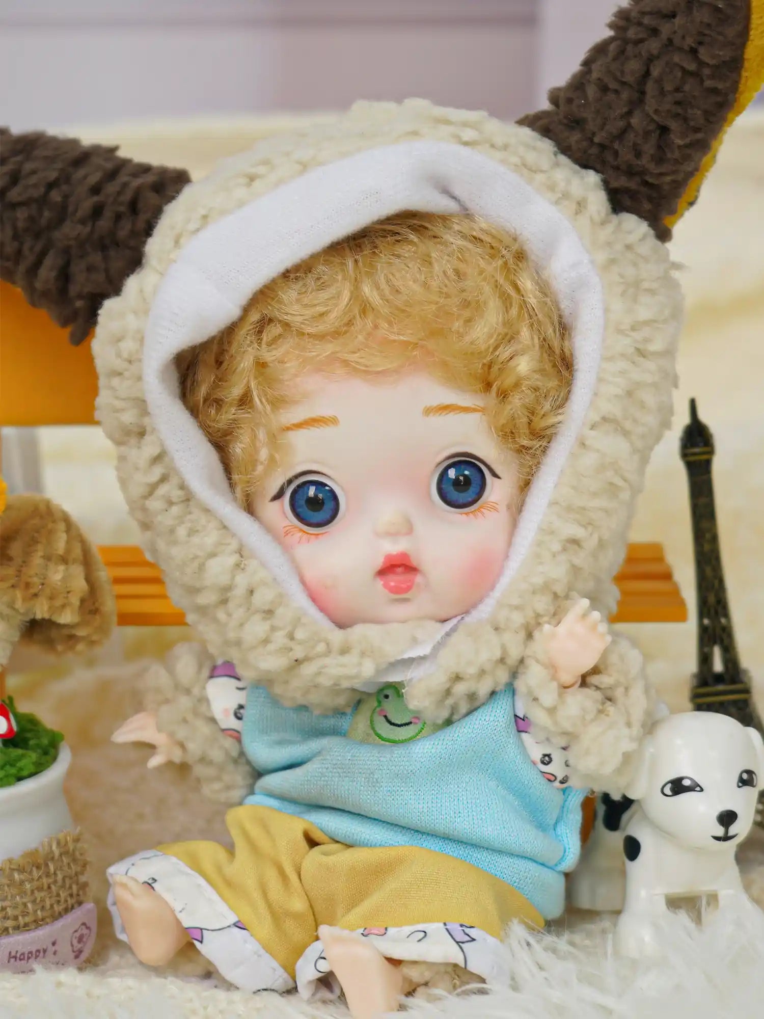 This BJD showcases a sheepish charm with its costume and is joined by a tiny Eiffel Tower and a porcelain puppy.