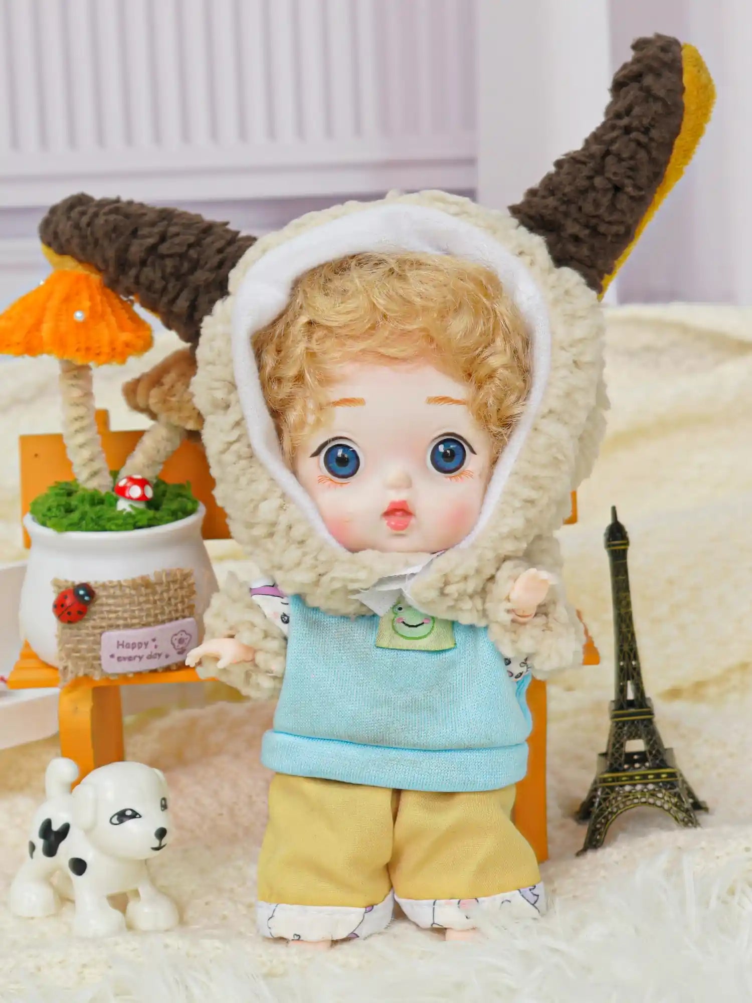 The BJD, complete with a cuddly lamb hood, shares a space with a delightful array of miniatures, including a symbolic Eiffel Tower.