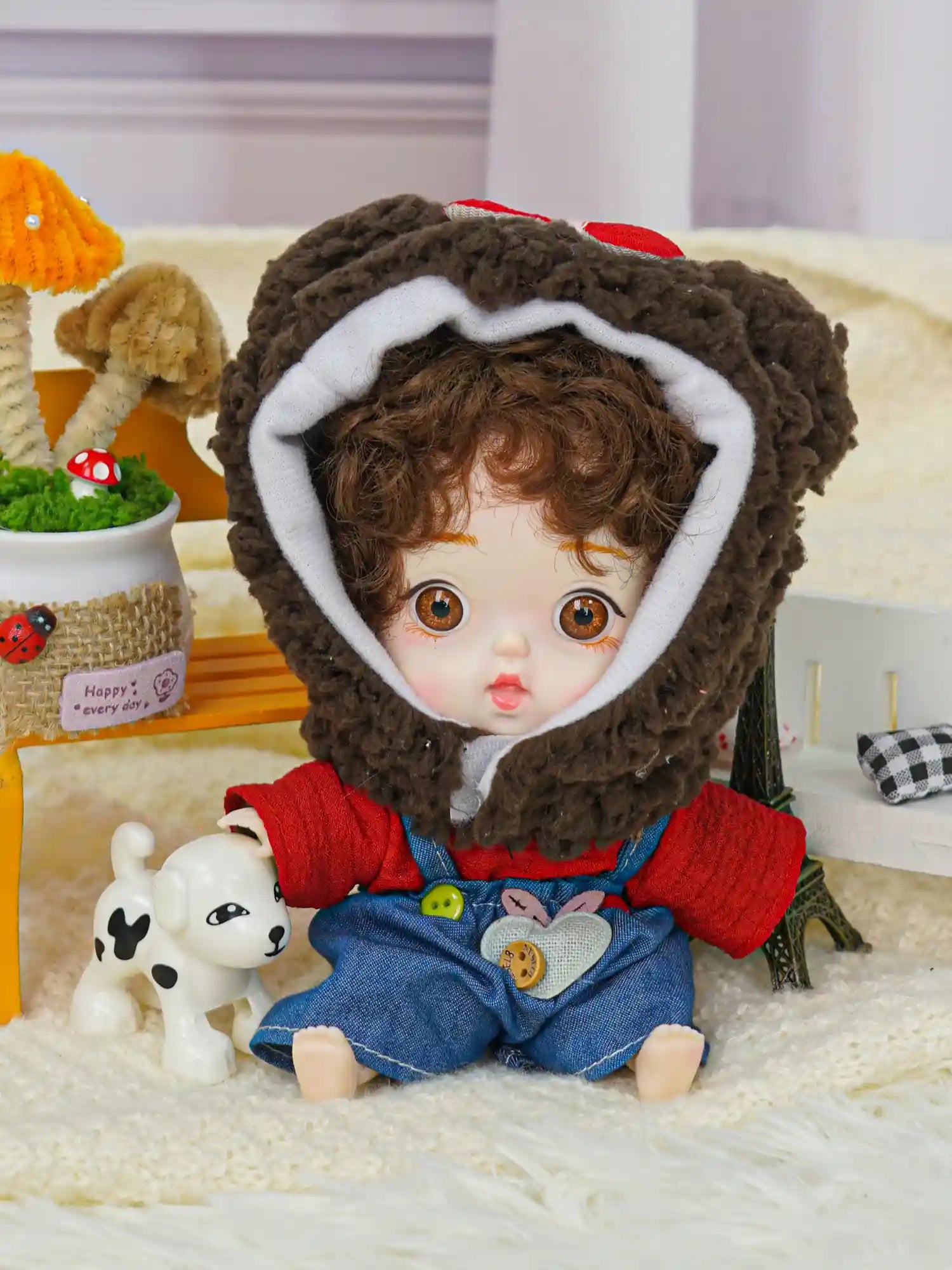 A charming doll with brown curls and a cuddly bear headpiece, flanked by a tiny Eiffel Tower and a toy canine.