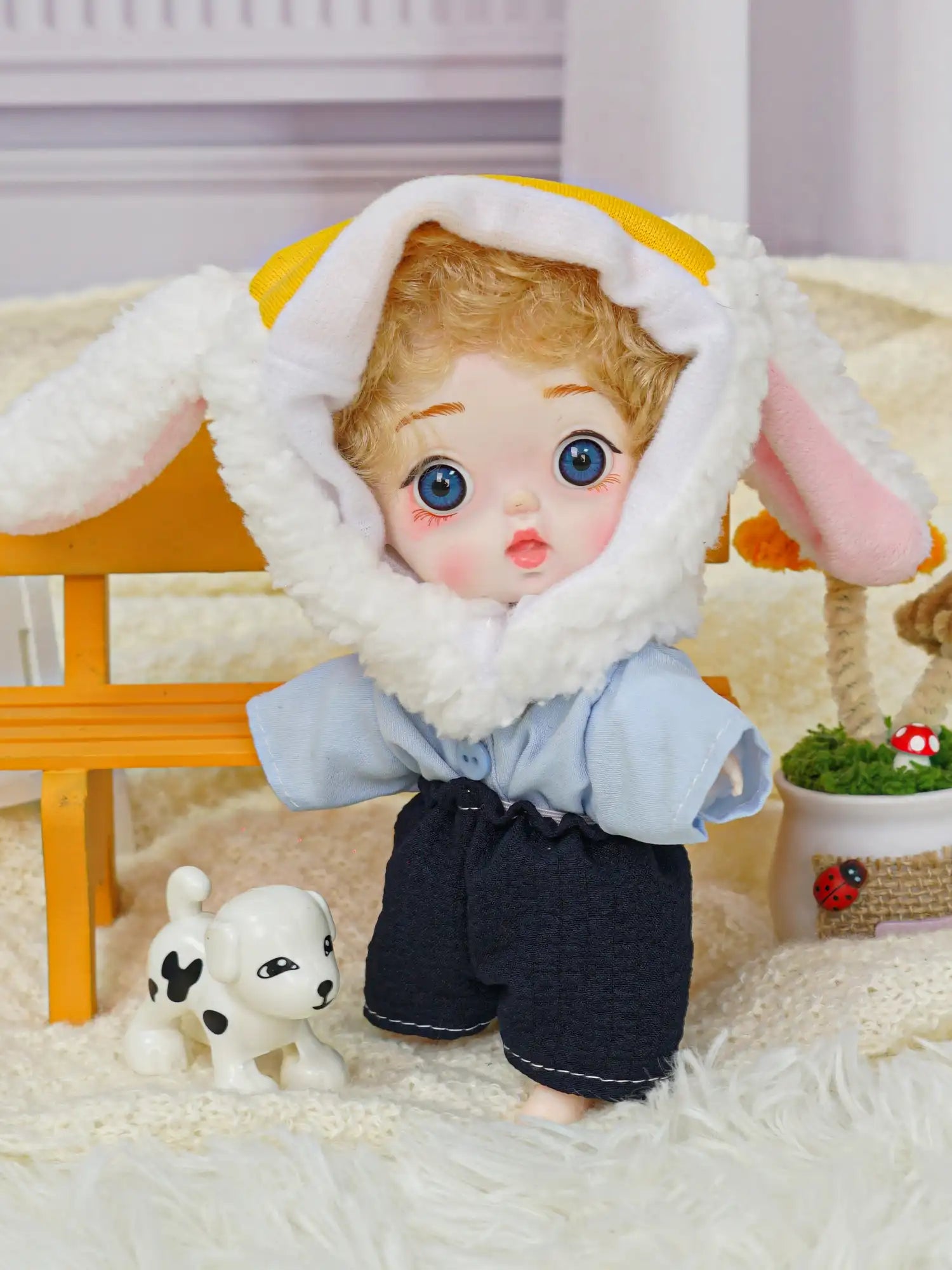 A charming doll with blue eyes and a lamb hood, seated next to a whimsical animal figure and colorful miniatures.