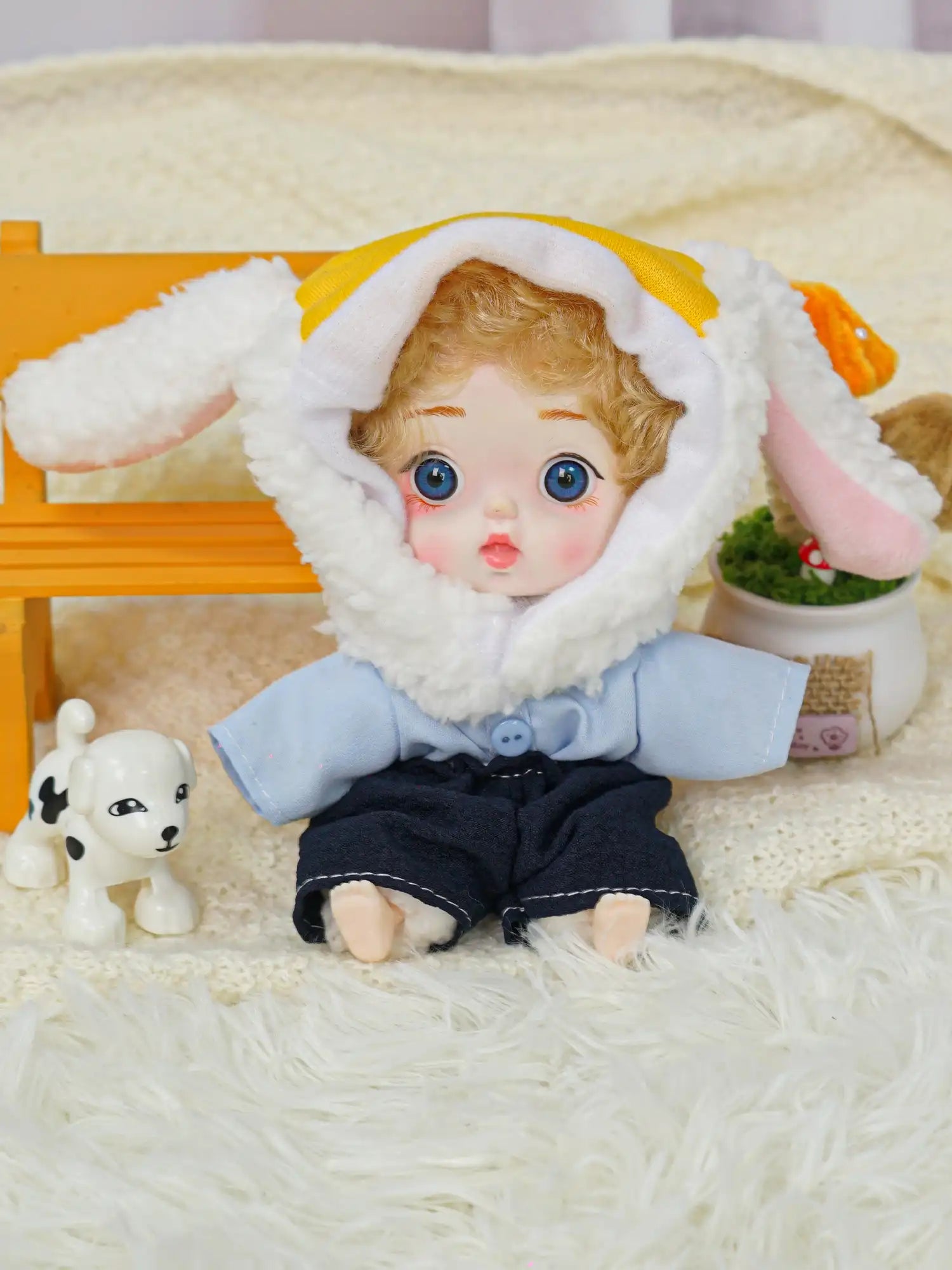 A blue-eyed doll with soft curly hair and a white lamb hood, accompanied by a miniature dog and cheerful ornaments.