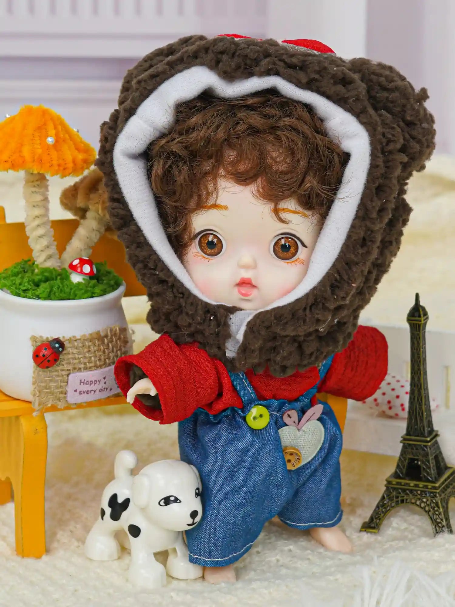 A delightful doll with a whimsical bear hat and denim overalls, accompanied by a little Eiffel Tower and a toy dog.