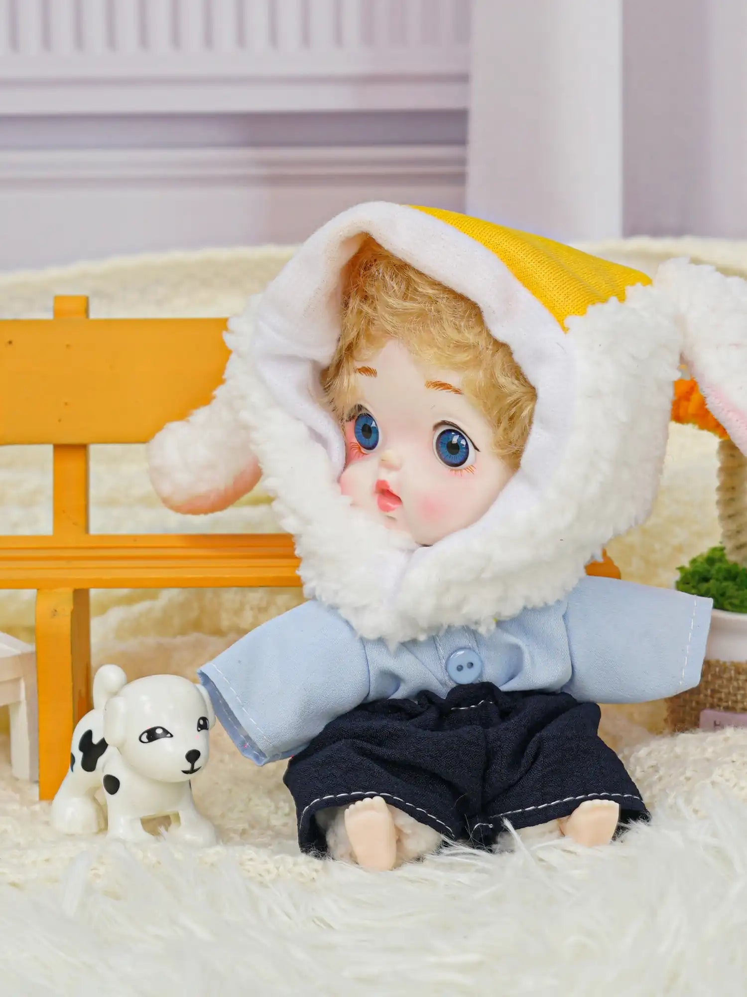 A sweet doll wearing a lamb hat with yellow trim, positioned near a tiny dog figure and delicate miniatures.