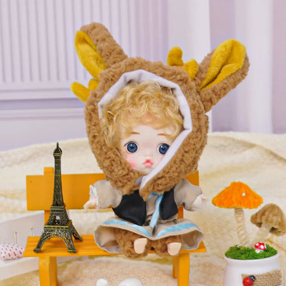 Charming curly-haired doll wearing a bunny costume, seated next to miniature Parisian and animal decorations.