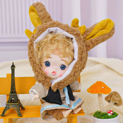 An adorable doll with blue eyes and a cozy bunny hat, situated among playful miniatures including a tiny Eiffel Tower.