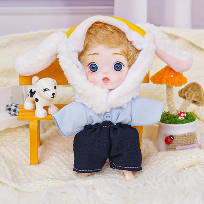 A charming doll with blue eyes and a lamb hood, seated next to a whimsical animal figure and colorful miniatures.