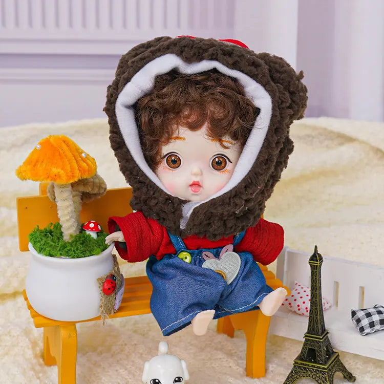 A brown-haired doll in a soft bear hood, with a petite Eiffel Tower model and a porcelain puppy by its side.