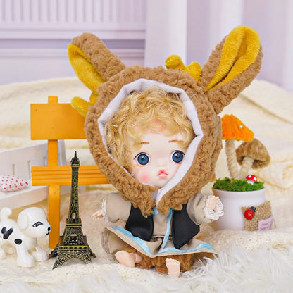  A golden-curled doll donning rabbit ears, with a miniature Eiffel Tower and animal friend beside it on a fluffy surface.