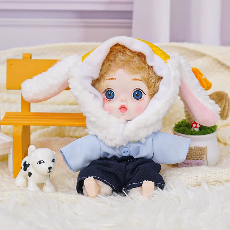 A blue-eyed doll with soft curly hair and a white lamb hood, accompanied by a miniature dog and cheerful ornaments.