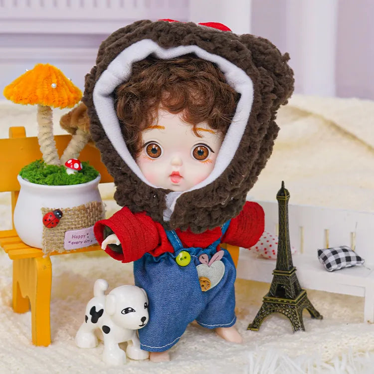 A brown-eyed doll wearing a cozy bear hood, displayed among a set of miniatures with a Parisian theme.