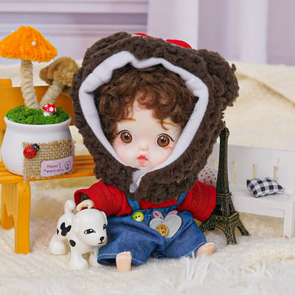 A cute doll with curly hair and a bear hood, standing next to a miniature Eiffel Tower and a white puppy toy.