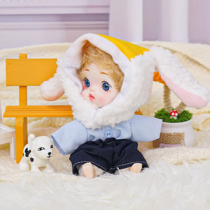 A sweet doll wearing a lamb hat with yellow trim, positioned near a tiny dog figure and delicate miniatures.