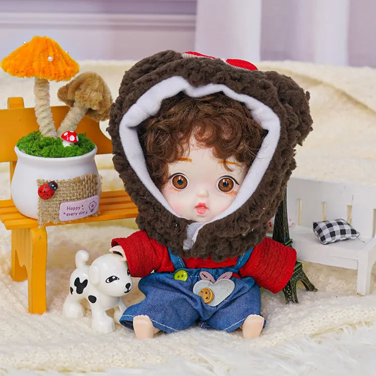 A charming doll with brown curls and a cuddly bear headpiece, flanked by a tiny Eiffel Tower and a toy canine.