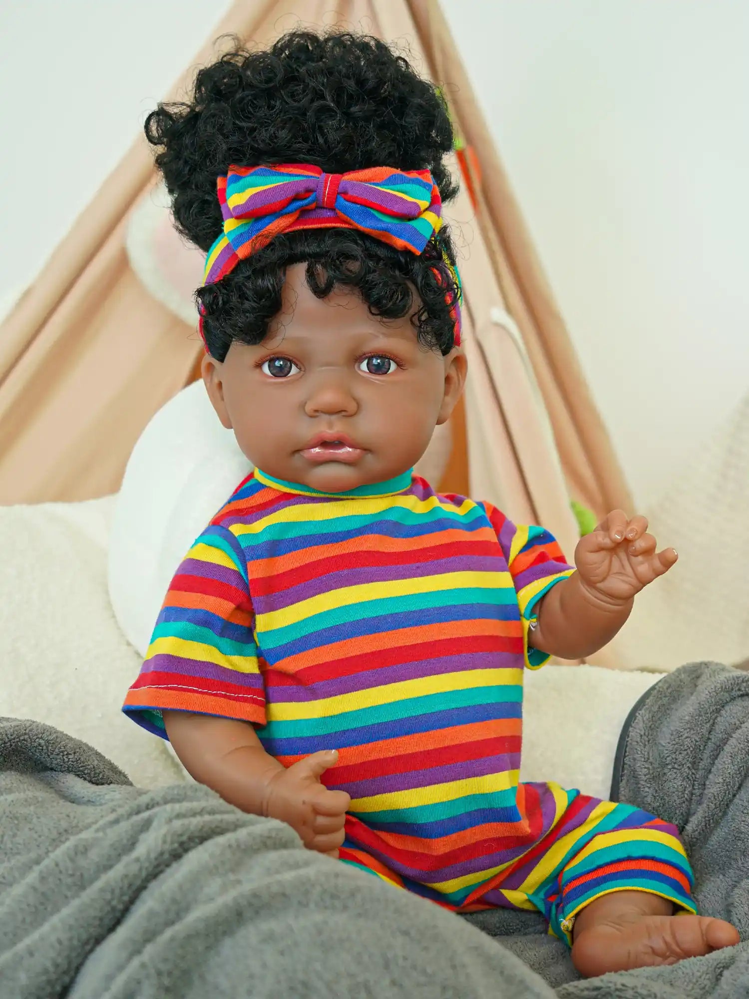 A black reborn baby doll sitting on a sofa wearing multi-colored striped clothes