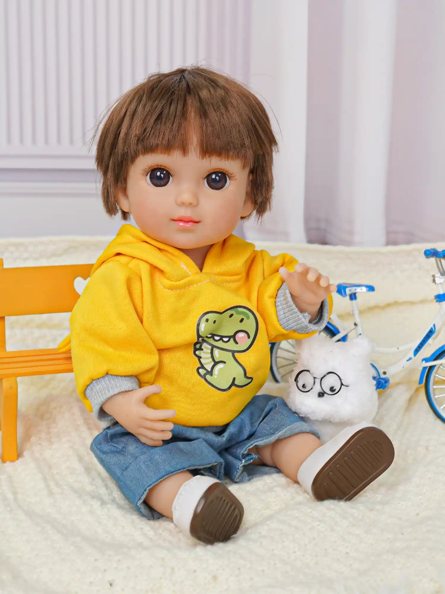 Seated doll with playful eyes, wearing a hoodie and jeans, next to a stuffed dog with glasses.