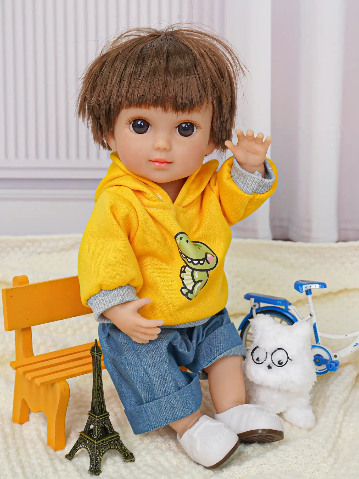 Doll with a short haircut, dressed in a sunny yellow sweatshirt, beside a white toy dog and bike.