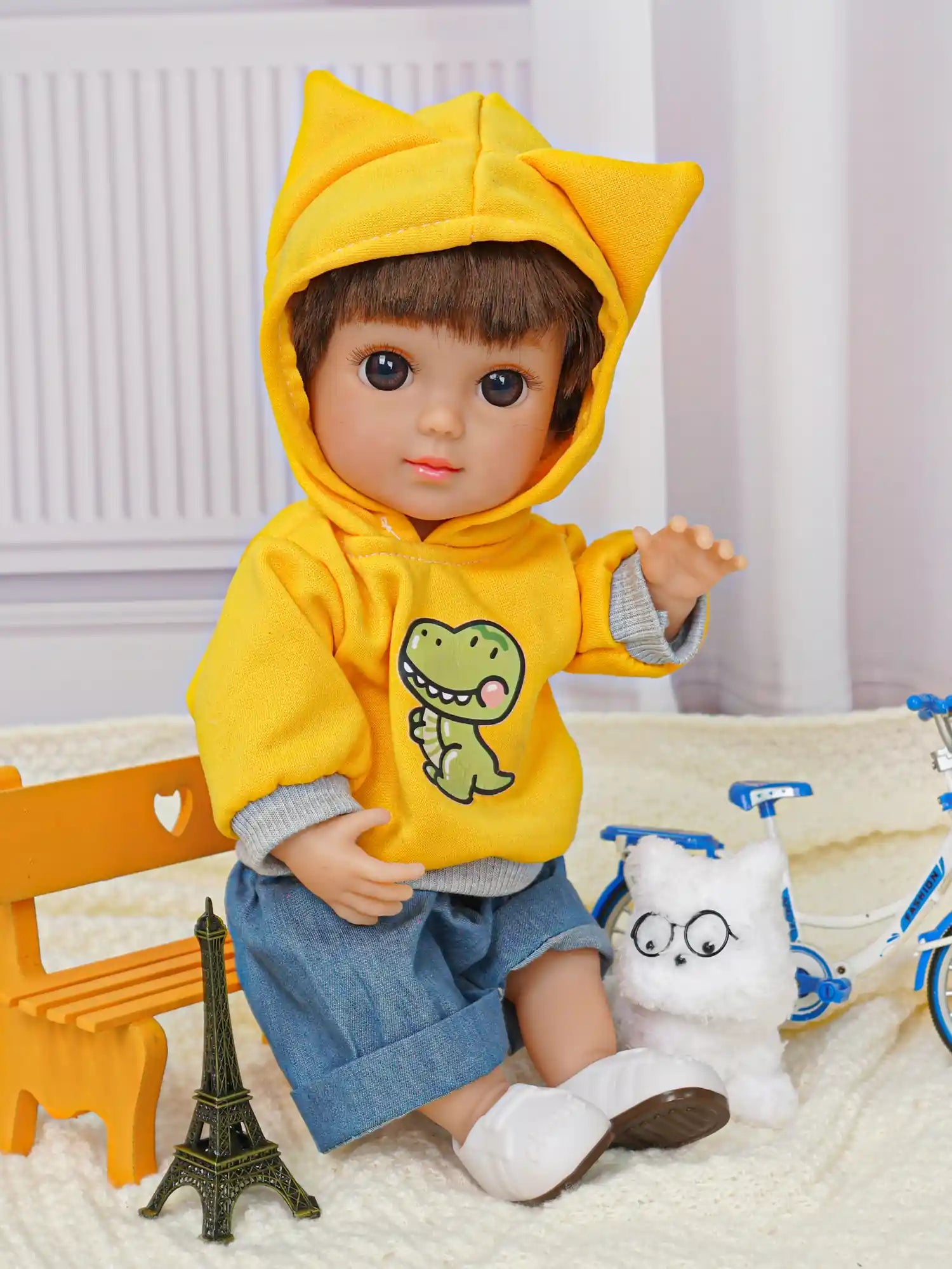 Doll with short brown hair in a yellow hoodie and denim shorts, with a plush dog and bicycle.