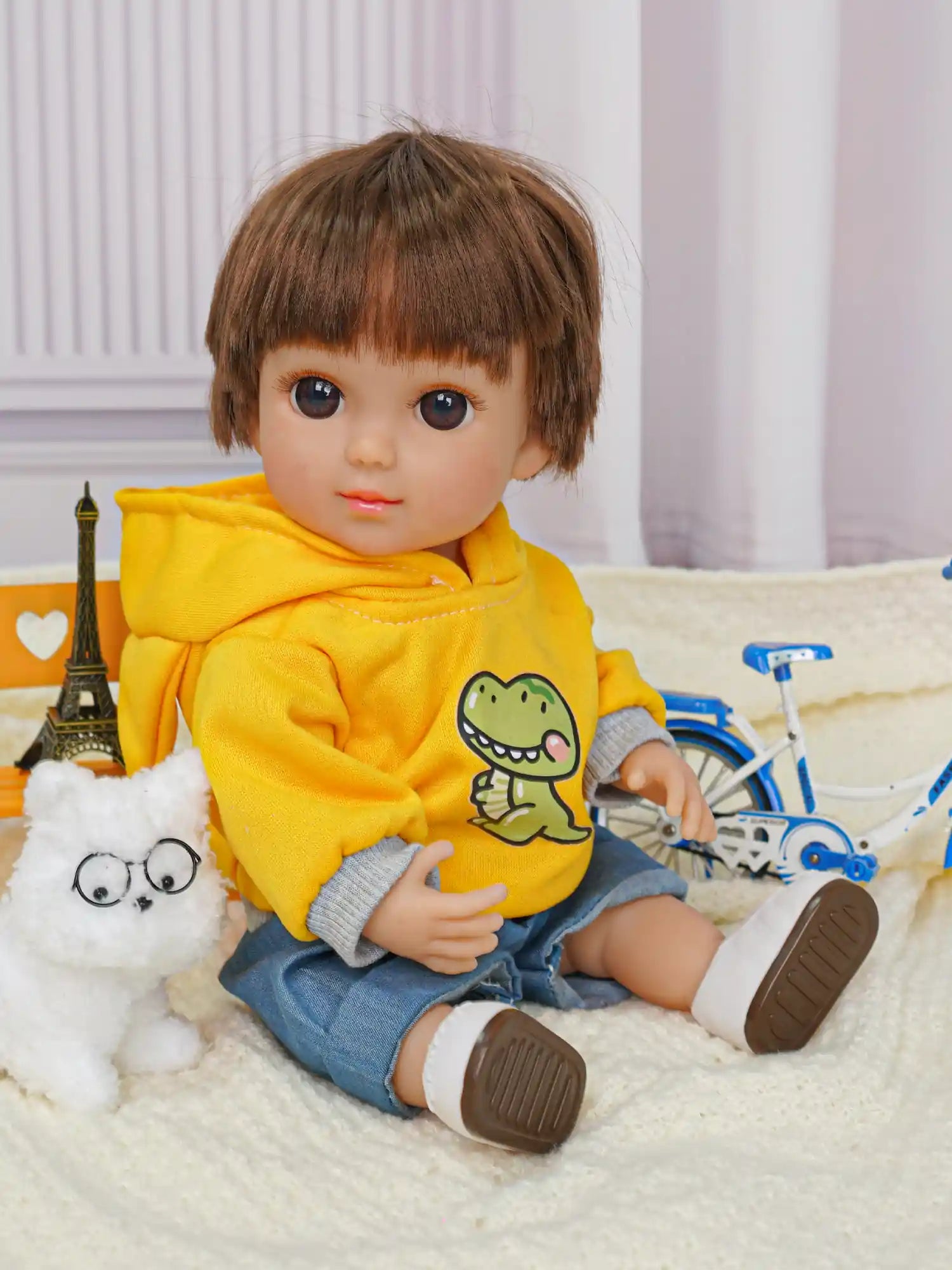 Smiling doll in yellow and denim, with a fluffy white dog and a small blue bicycle.