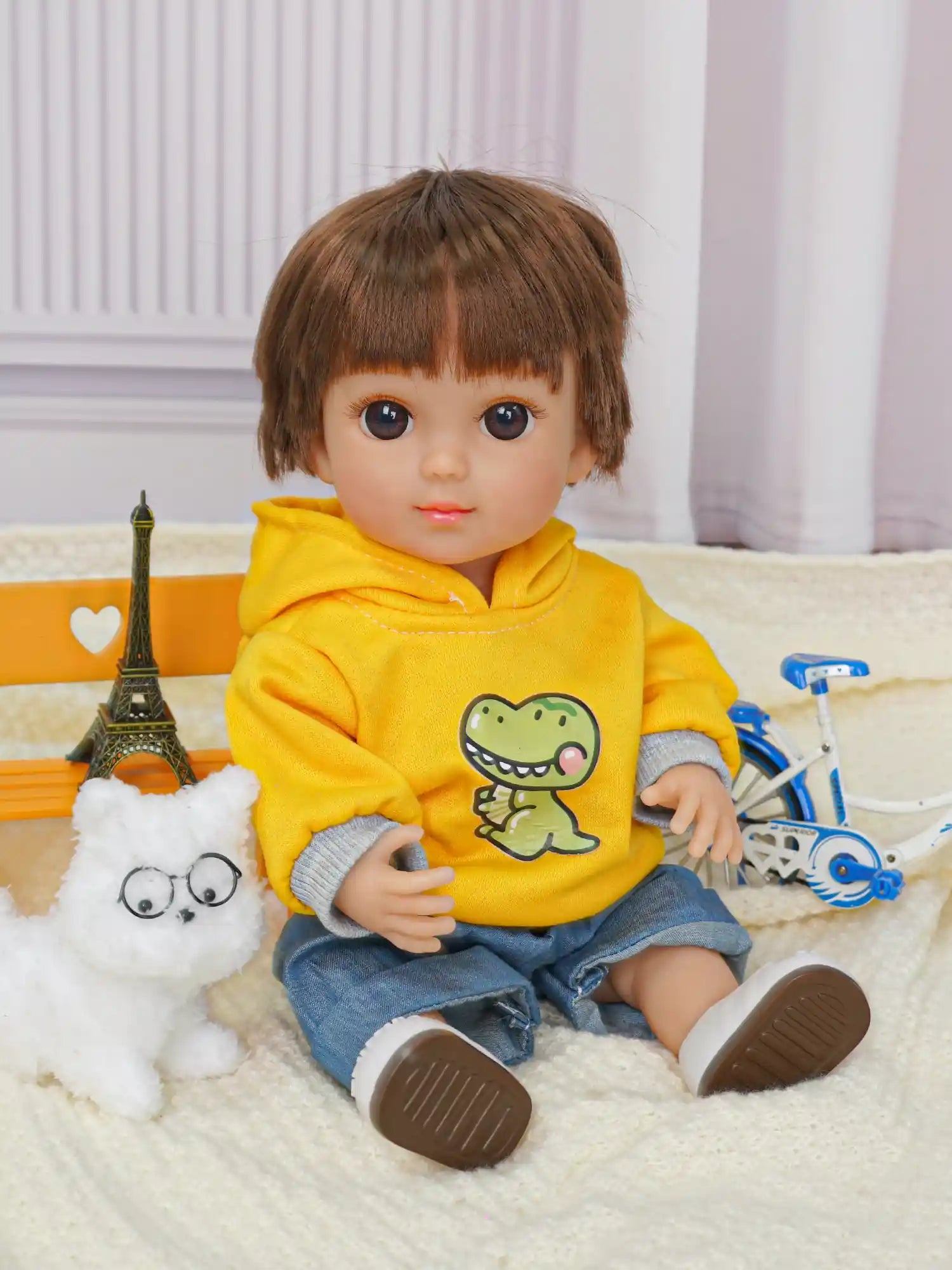Casual doll with a dinosaur on its sweatshirt, beside a fluffy dog toy and a toy bike.