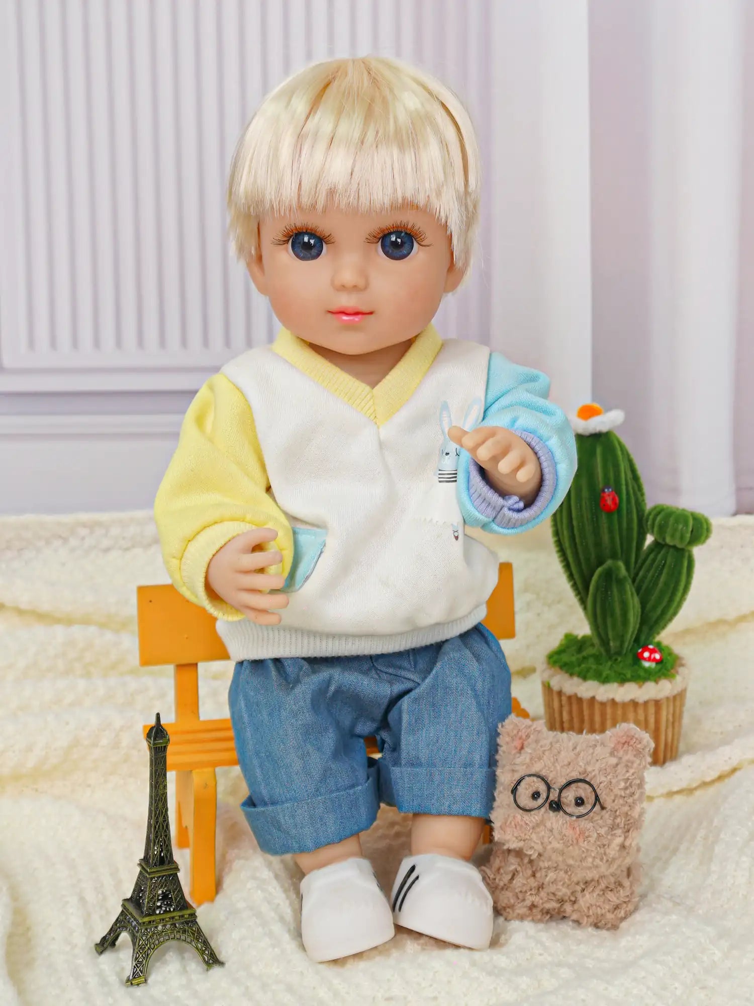 Blonde doll with blue eyes, yellow cardigan, and denim pants, seated by a toy Eiffel Tower.