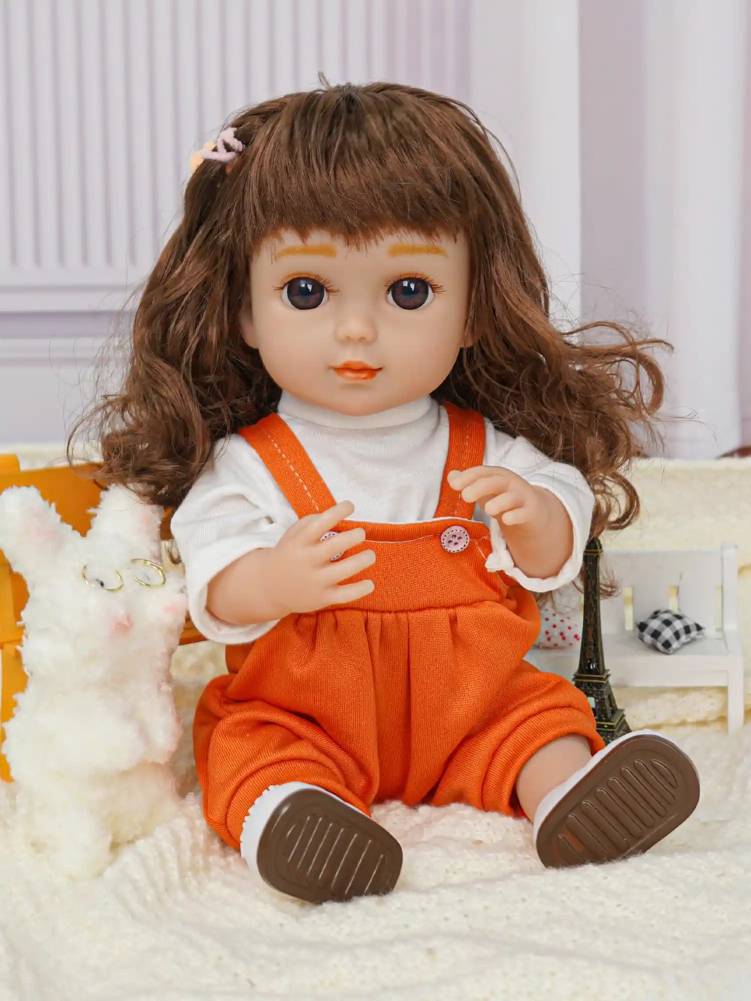 Doll with wavy hair and playful expression, next to a fluffy toy dog and a small Eiffel Tower.
