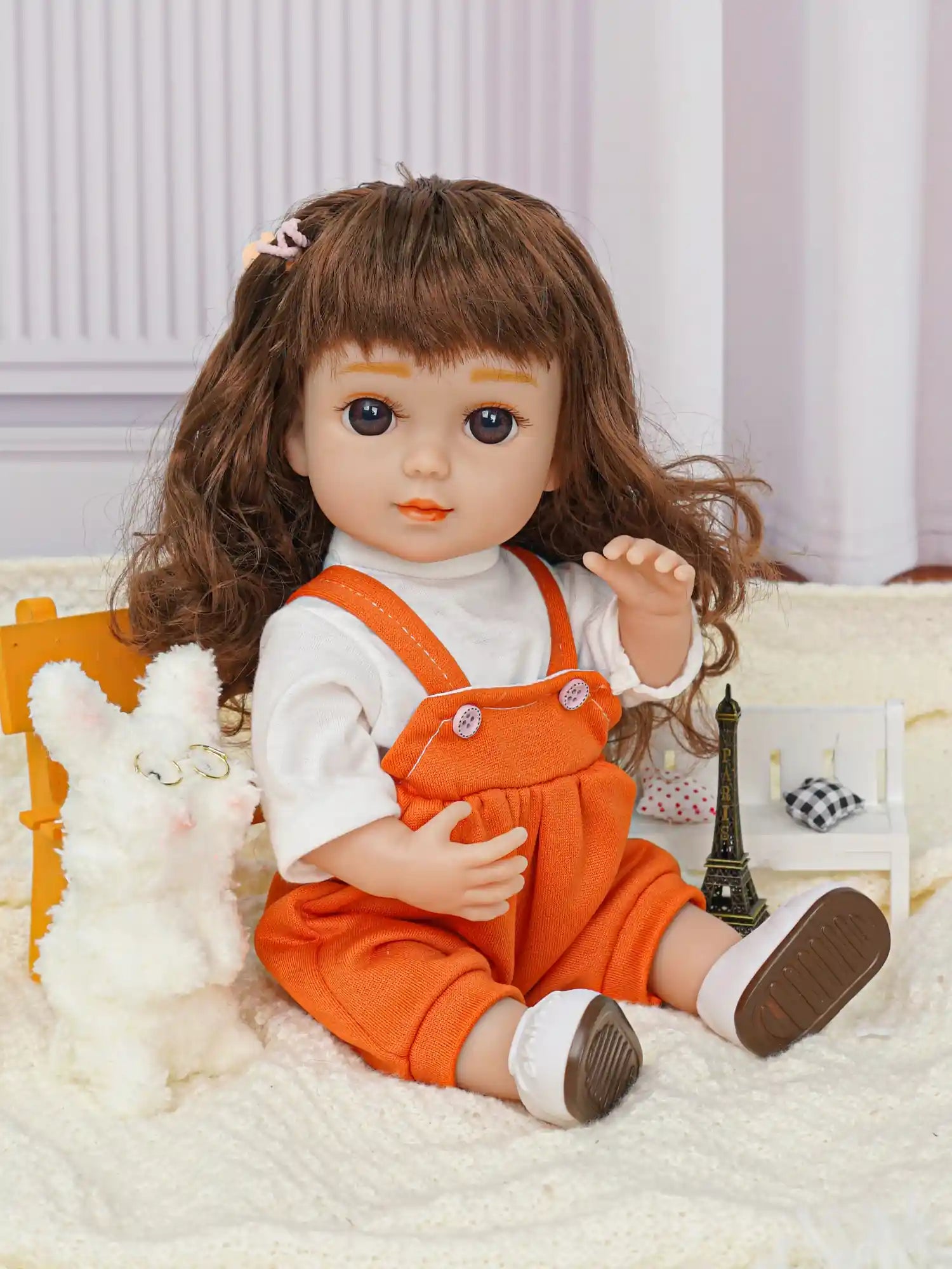 Childlike doll with brown curls, dressed in orange, with a stuffed dog and metal Eiffel Tower.