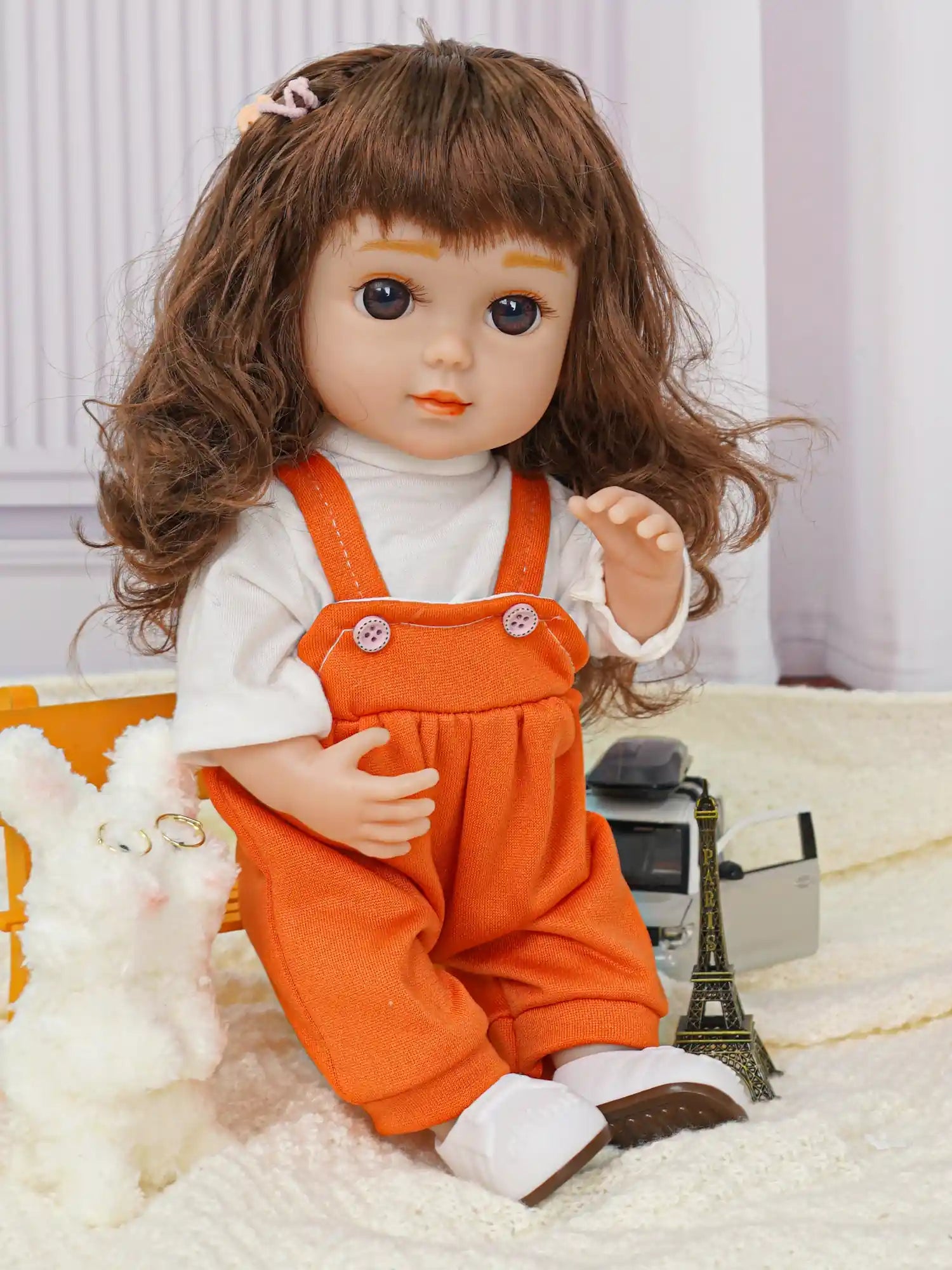 Doll with hair clip, orange dungarees, white dog toy, and Eiffel Tower model.