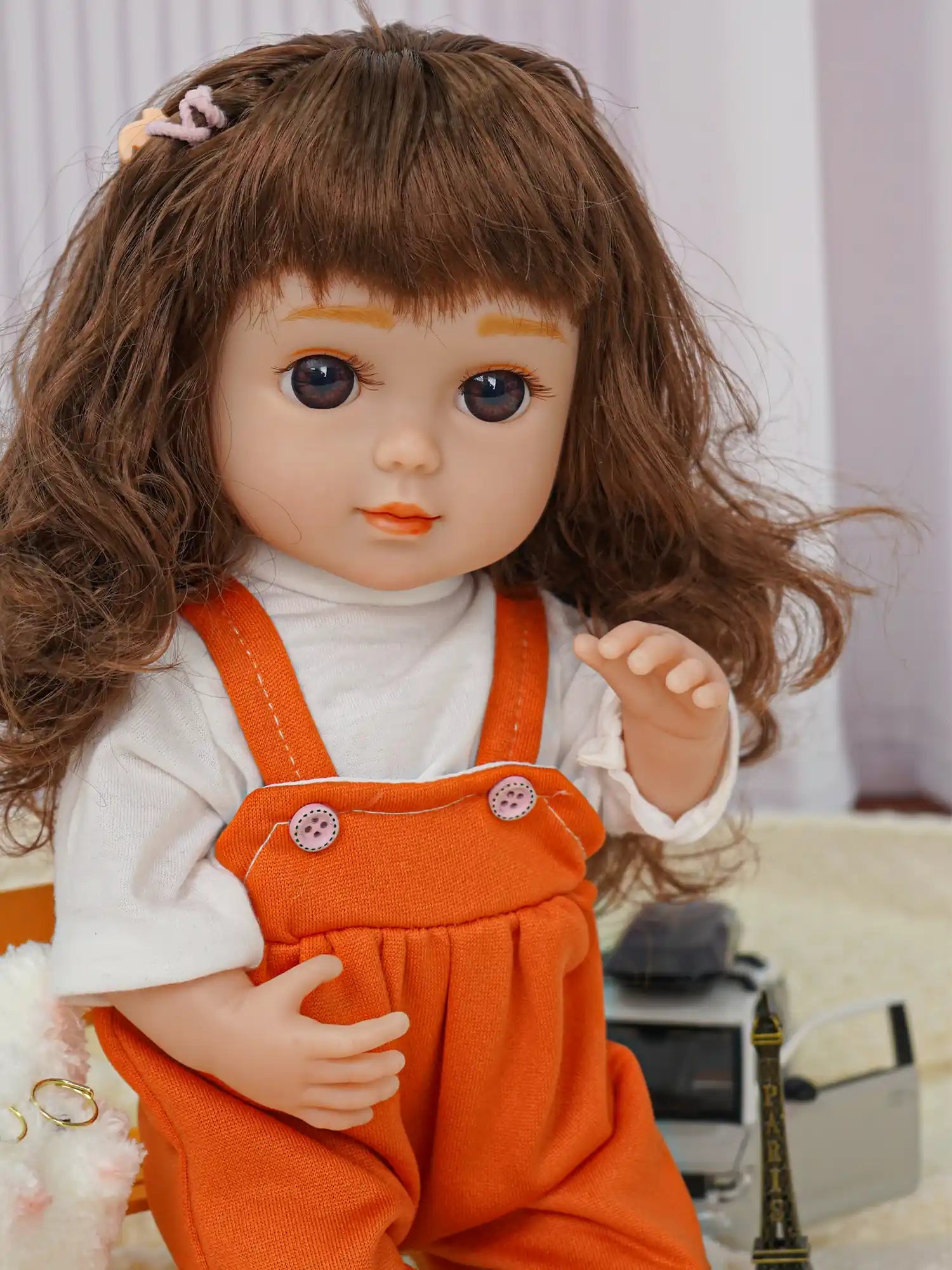 Seated doll with wavy hair, white and orange outfit, next to a plush dog and Paris landmark.