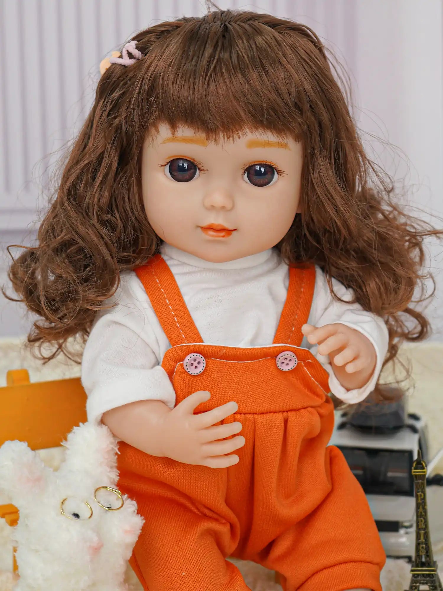 Doll in orange jumpsuit, sitting with a white plush dog and a toy camera.