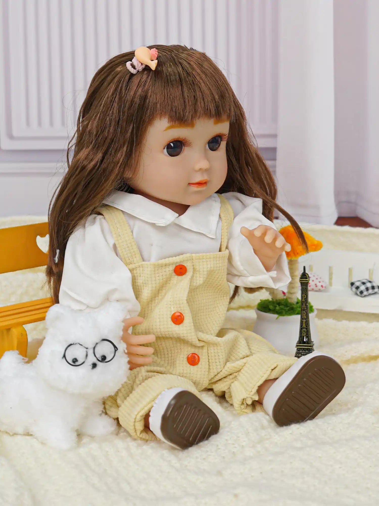 Doll with blue eyes, dressed in overalls, sitting by a toy dog and a metal tower.
