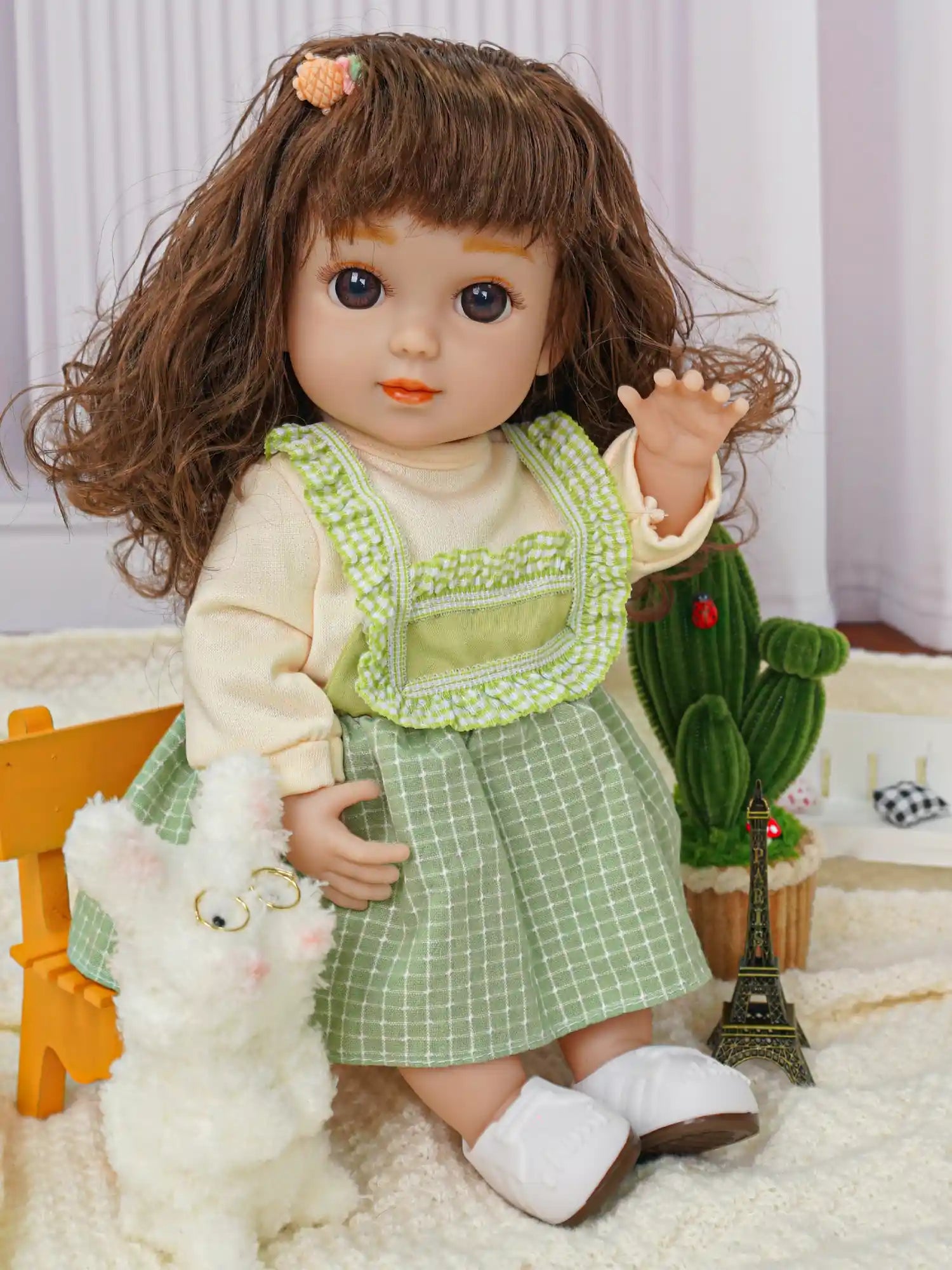 Doll in a green pinafore dress, waving, with fluffy dog toys and indoor plant.
