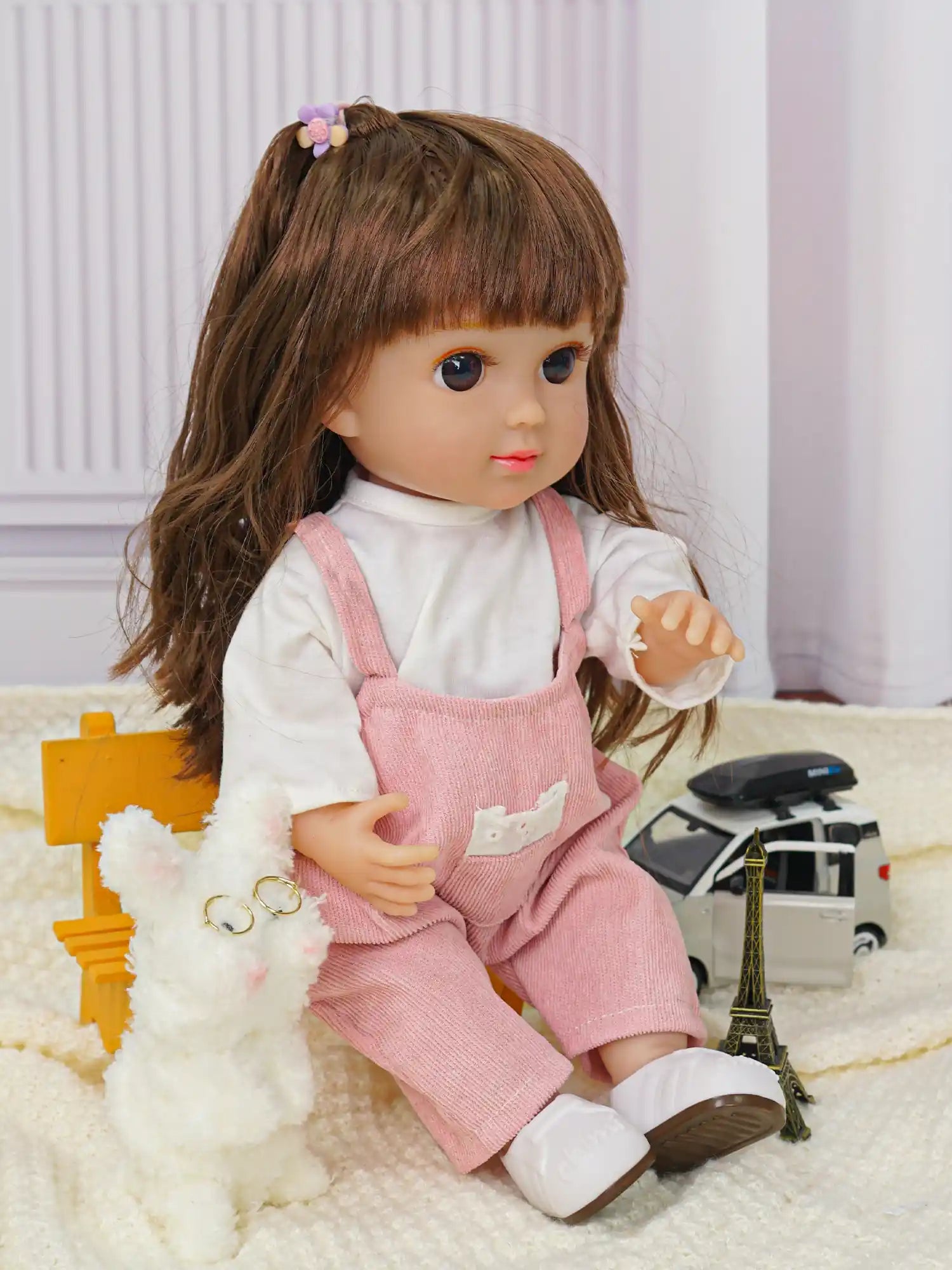 Doll seated on a chair with a white plush dog and toy Eiffel Tower.