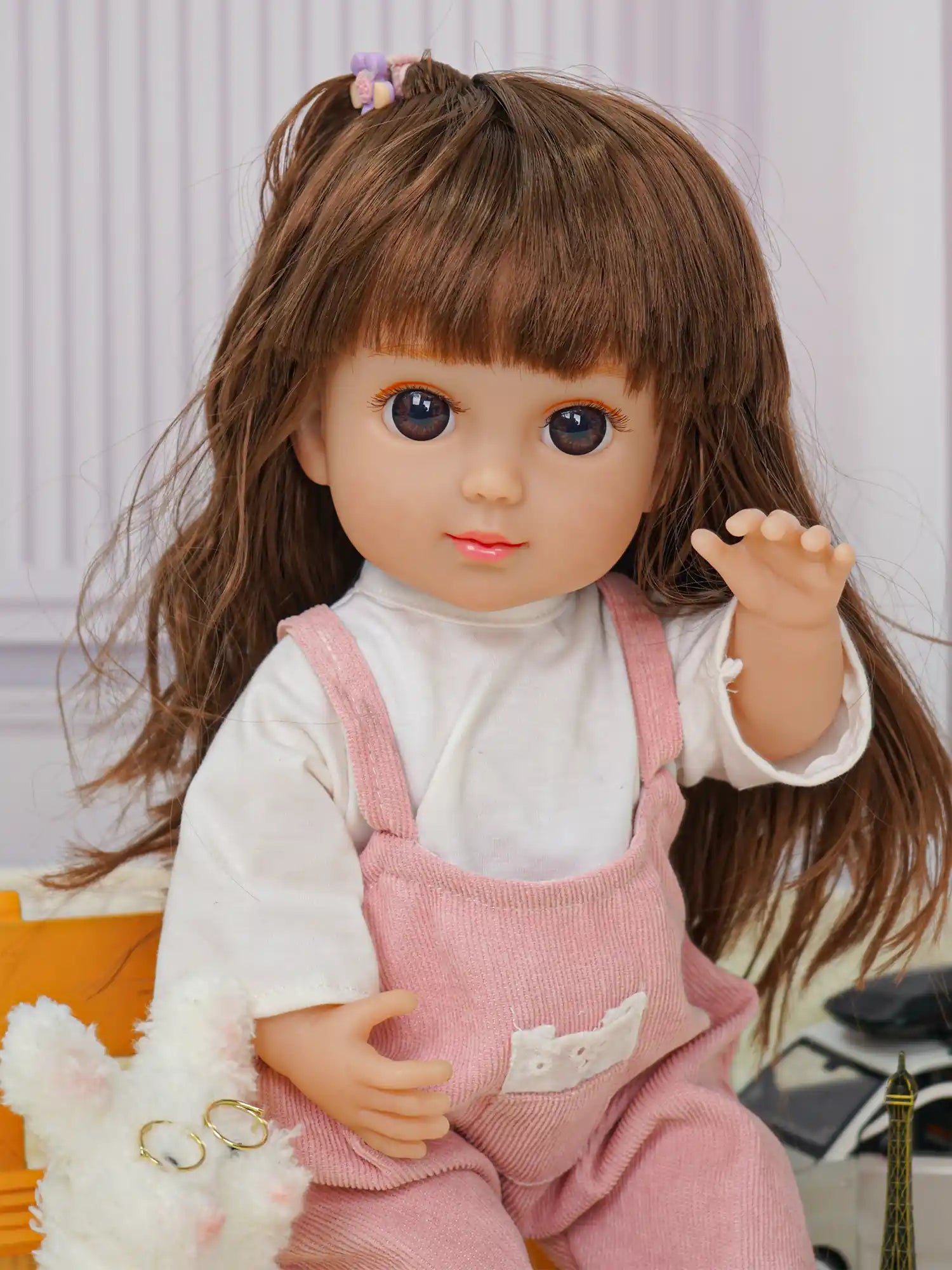 Doll with brunette ponytail, pink overalls, plush dog, and Eiffel Tower figurine.