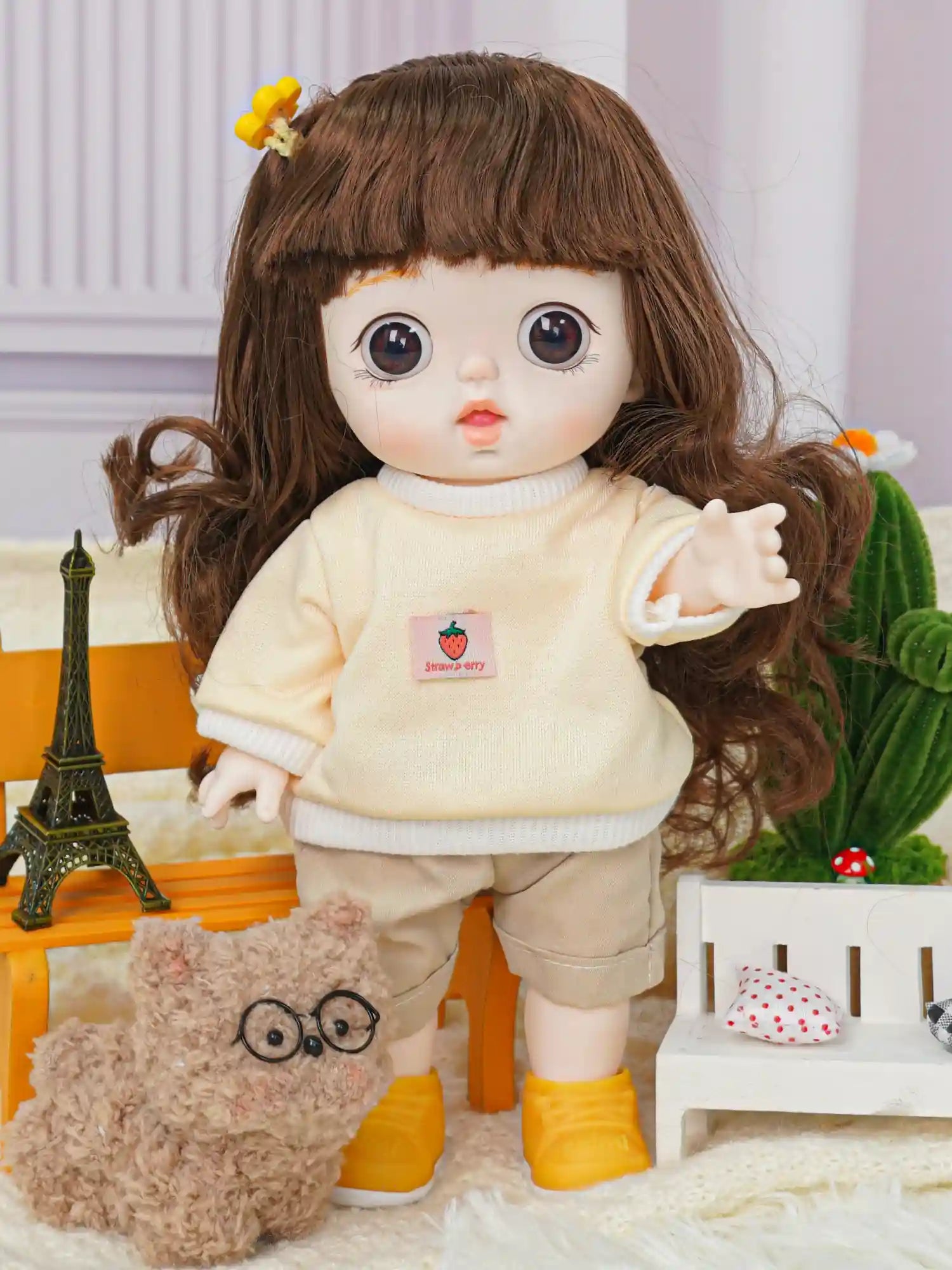 A doll with expressive brown eyes and lush hair, wearing a cream sweater and beige pants, poses with a cactus.