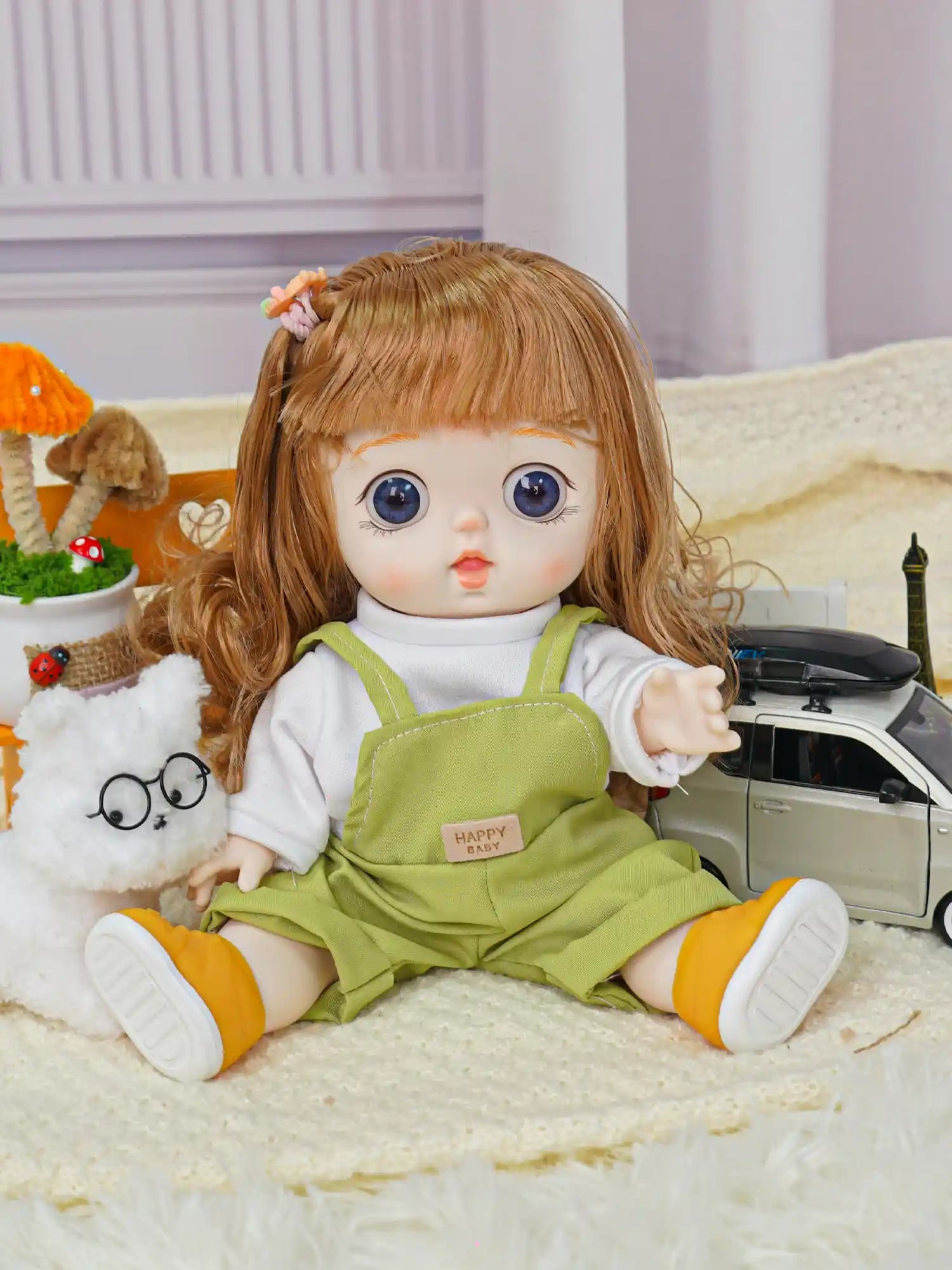A friendly-faced doll with overalls and toy accessories, including a fluffy white cat and miniature vehicle.
