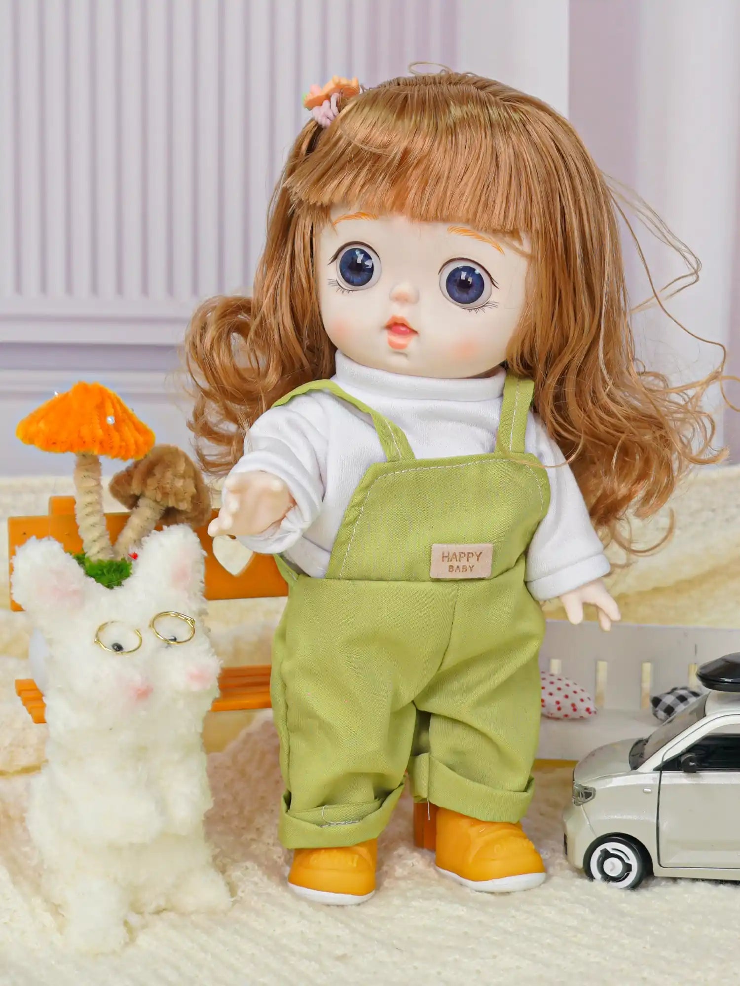 Doll with chestnut hair and blue eyes in a white shirt and green overalls, next to a fluffy toy cat.