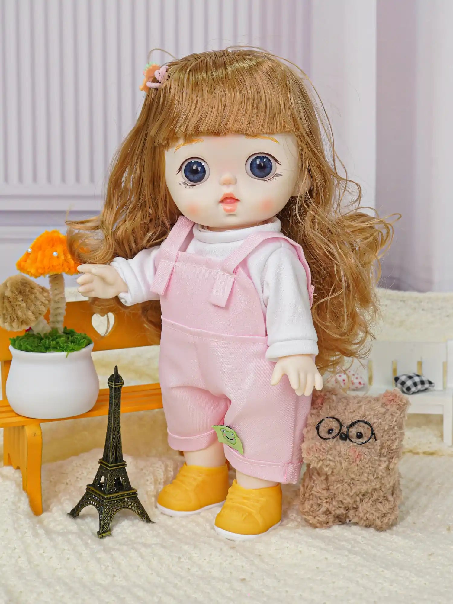 A doll with light brown hair and striking blue eyes wearing a pink pinafore over a white shirt, standing with a plush toy.