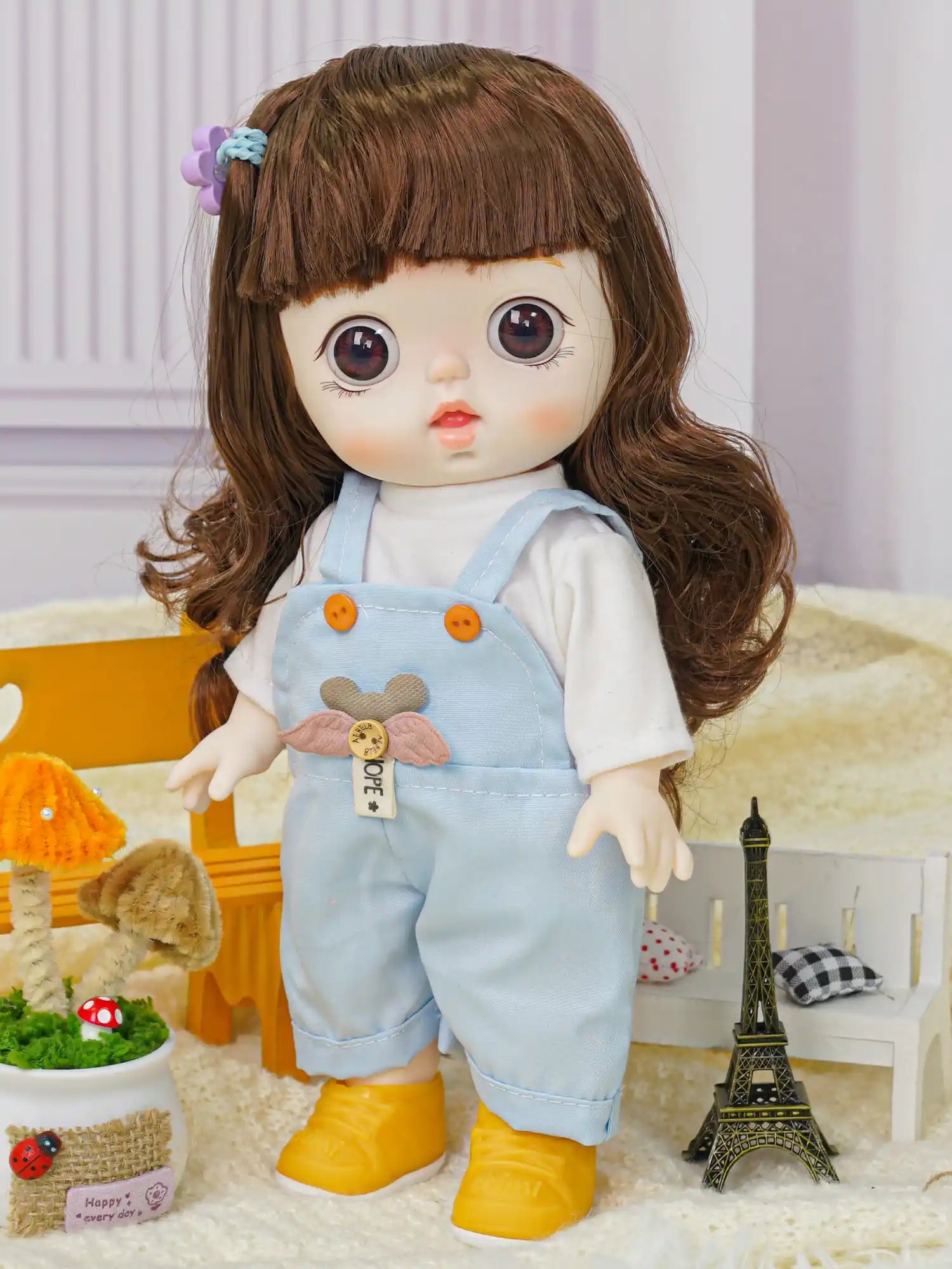A brunette doll with lifelike eyes, dressed in cute overalls, in a setup with playful mushroom decor and a Parisian touch.