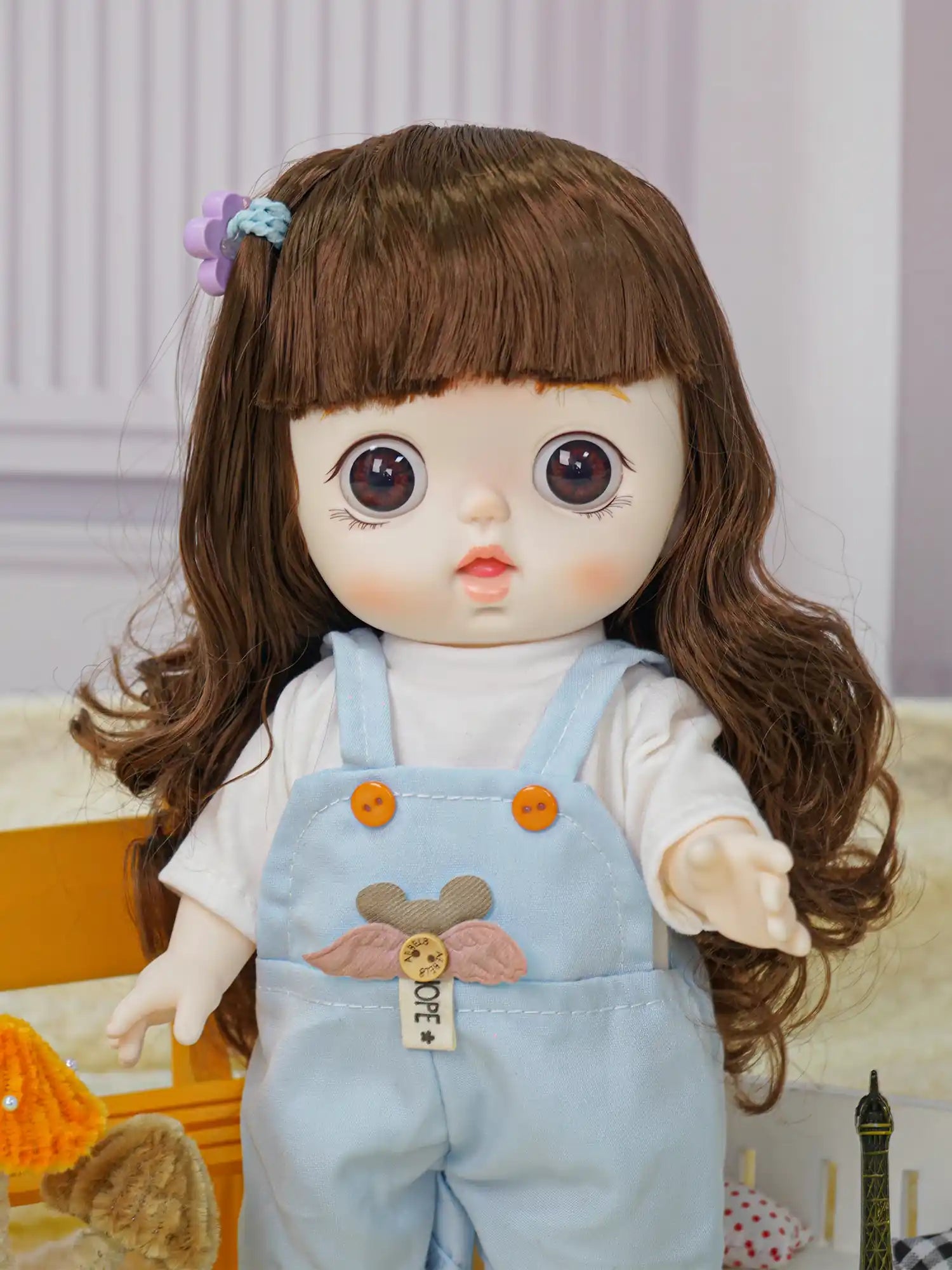 Toy doll with a whimsical look, dressed in light blue overalls and standing next to a tiny replica of the Eiffel Tower.