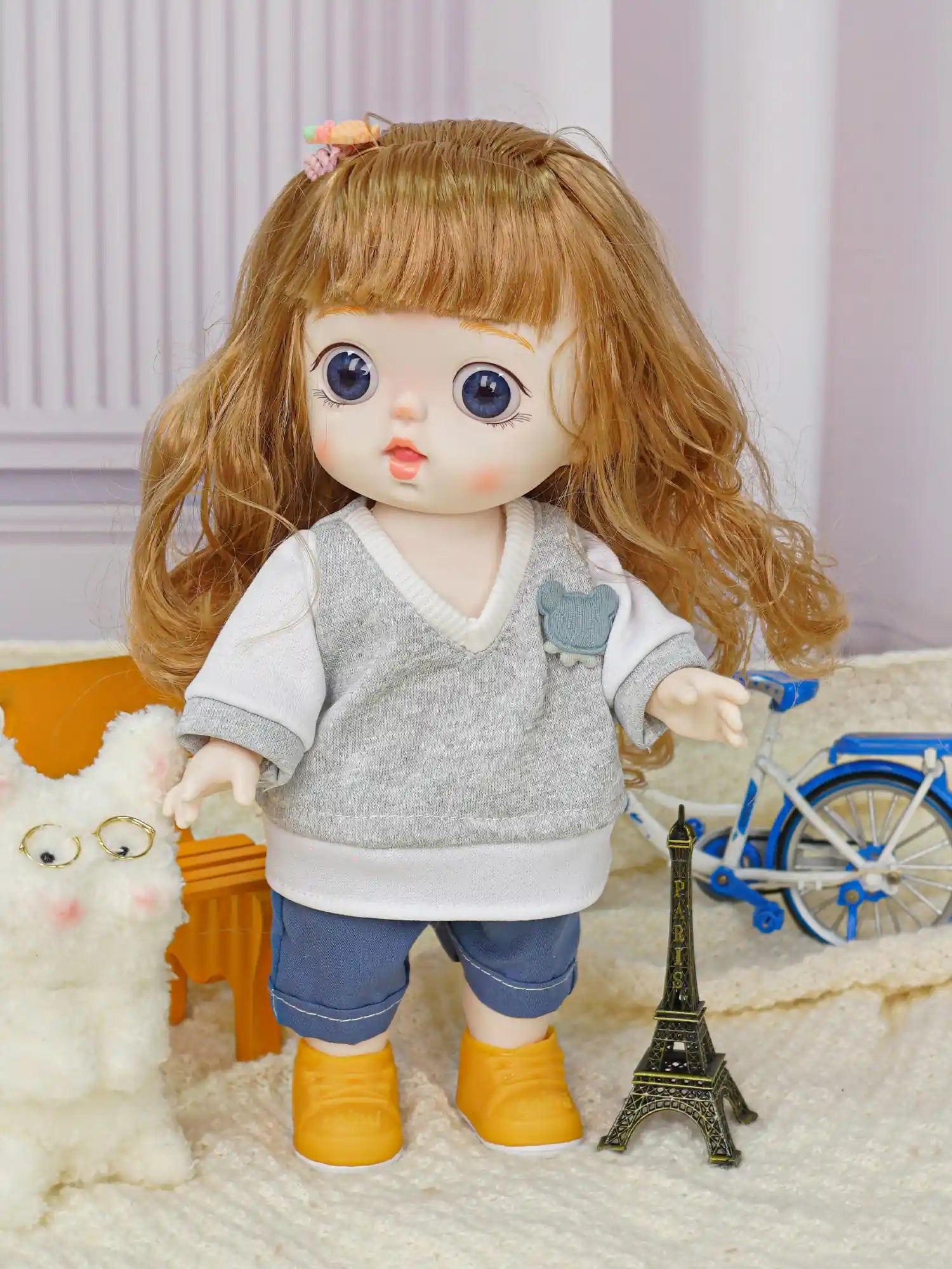 Cute doll in modern attire with a pet plush, against a backdrop of miniature furniture and a toy bike.