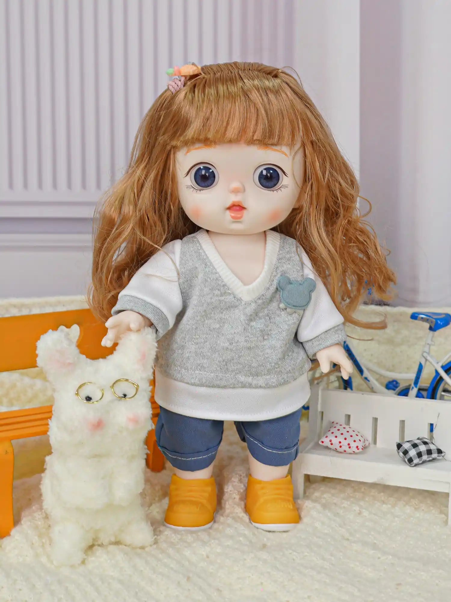 A doll with brown wavy hair and blue eyes, dressed in a gray sweater and blue jeans, stands next to a fluffy white toy dog with glasses.