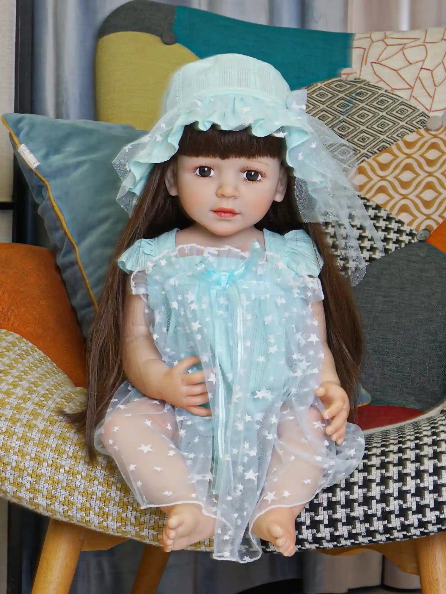 Doll with long brown hair and aqua hat, seated in a star-patterned tulle dress.